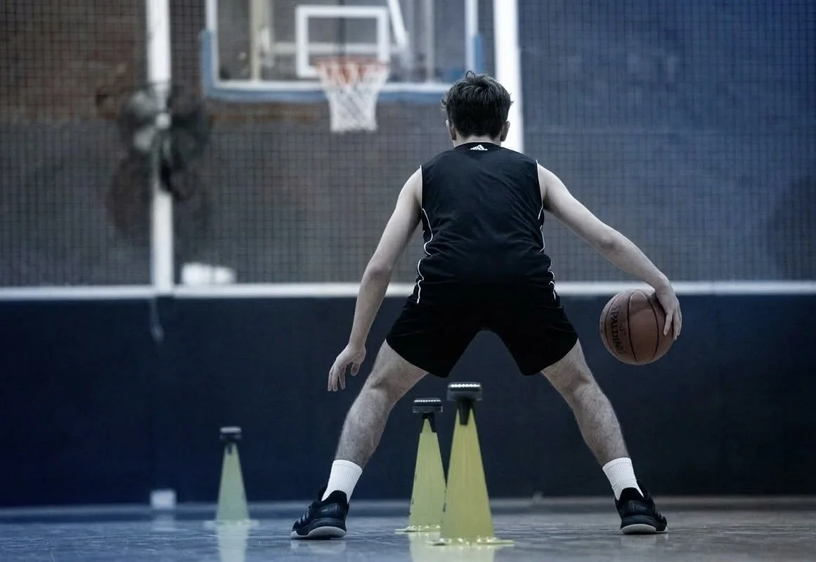 Middle school basketball player practicing technical crossover dribbling through cones in an Austin gym.