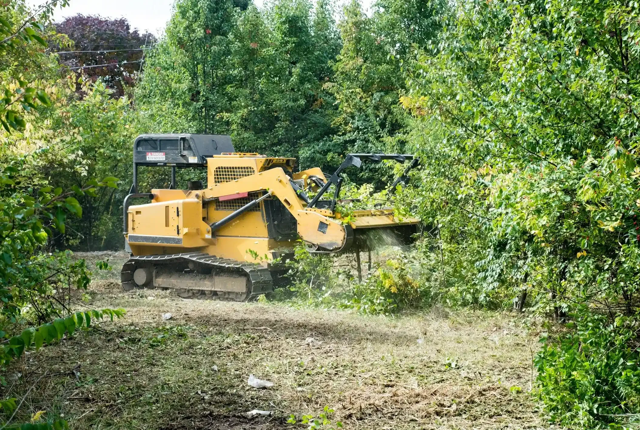 A yellow bulldozer clearing vegetation on a dirt path in a forested area.