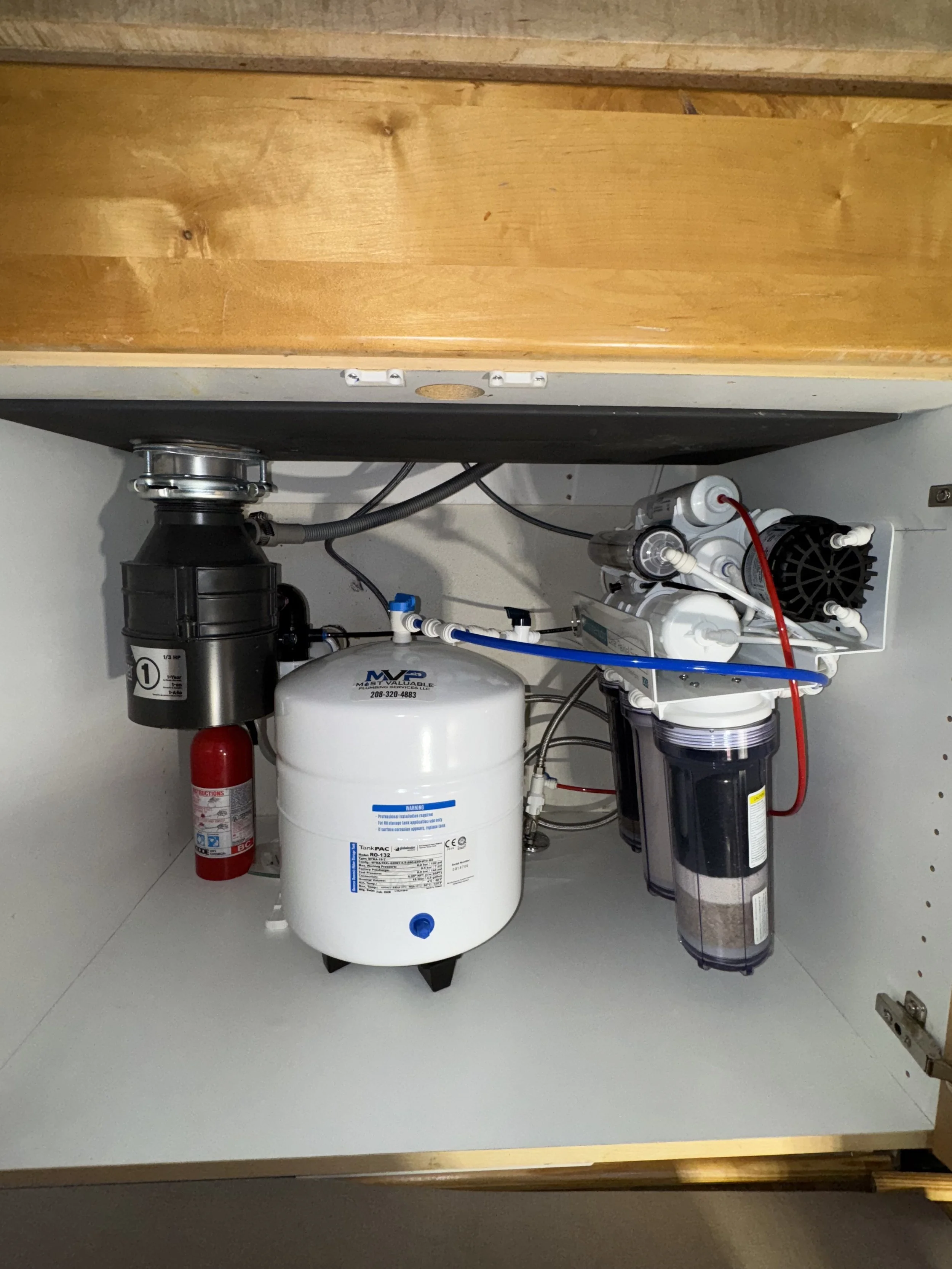 Under-sink water filtration system with filter and pump, installed in a kitchen cabinet with garbage disposal.