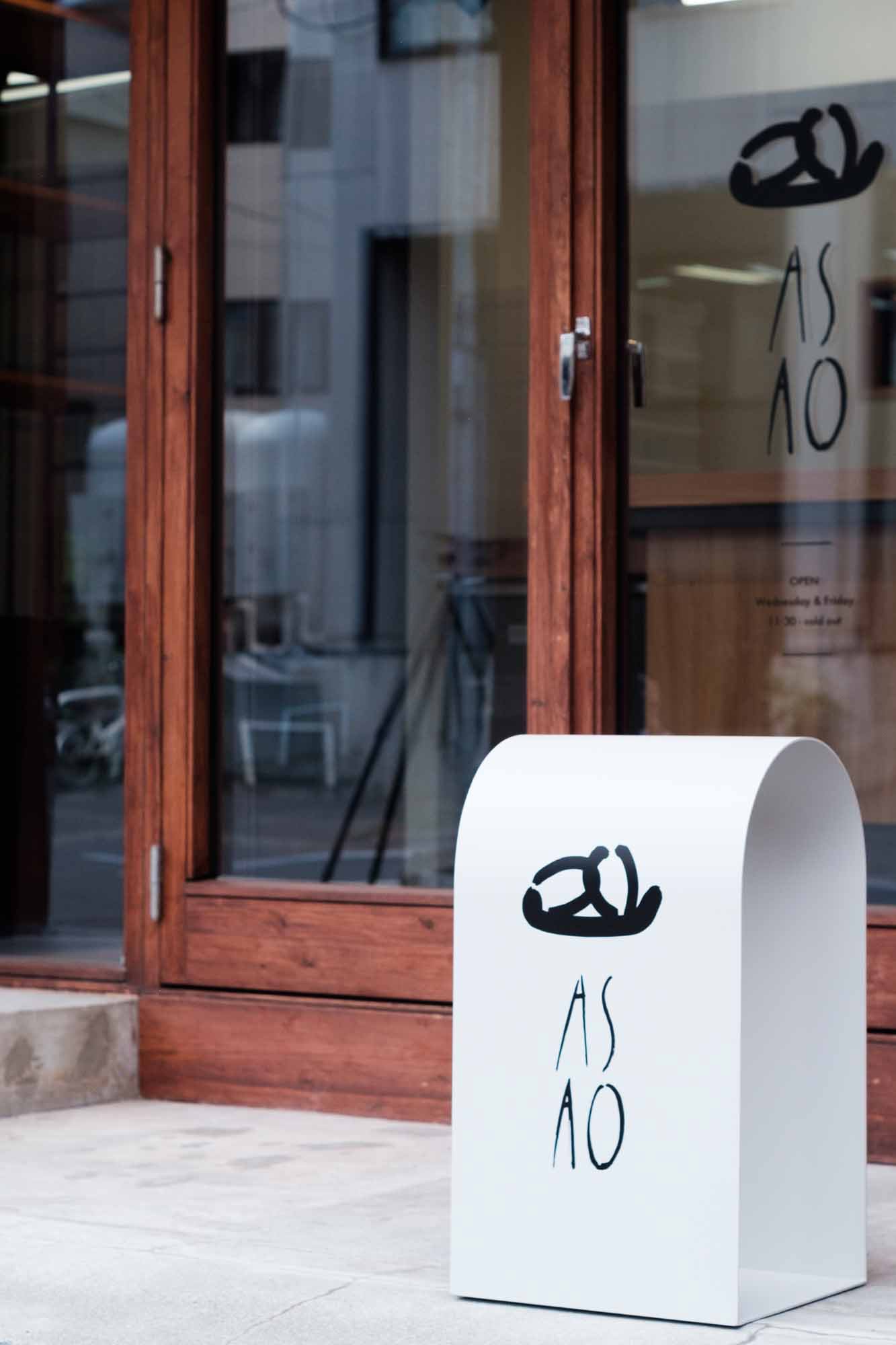 白いスタンドサインと店舗入口に設置されたロゴマーク。White freestanding sign with ASAO logo at the bakery entrance.