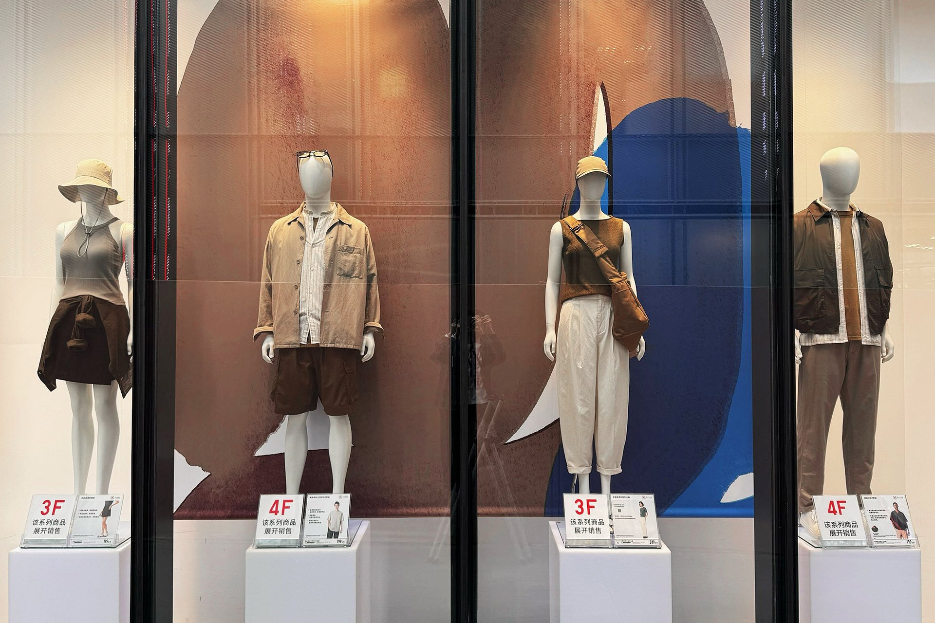 UNIQLO中国の店舗ディスプレイ。ブラウンとブルーのアートを背景に、ナチュラルカラーのスタイルを提案(2025年春夏、アート:サトウアサミ)UNIQLO China window display featuring natural-toned fashion in front of brown and blue abstract art for 2025 S/S collection by Asami Sato