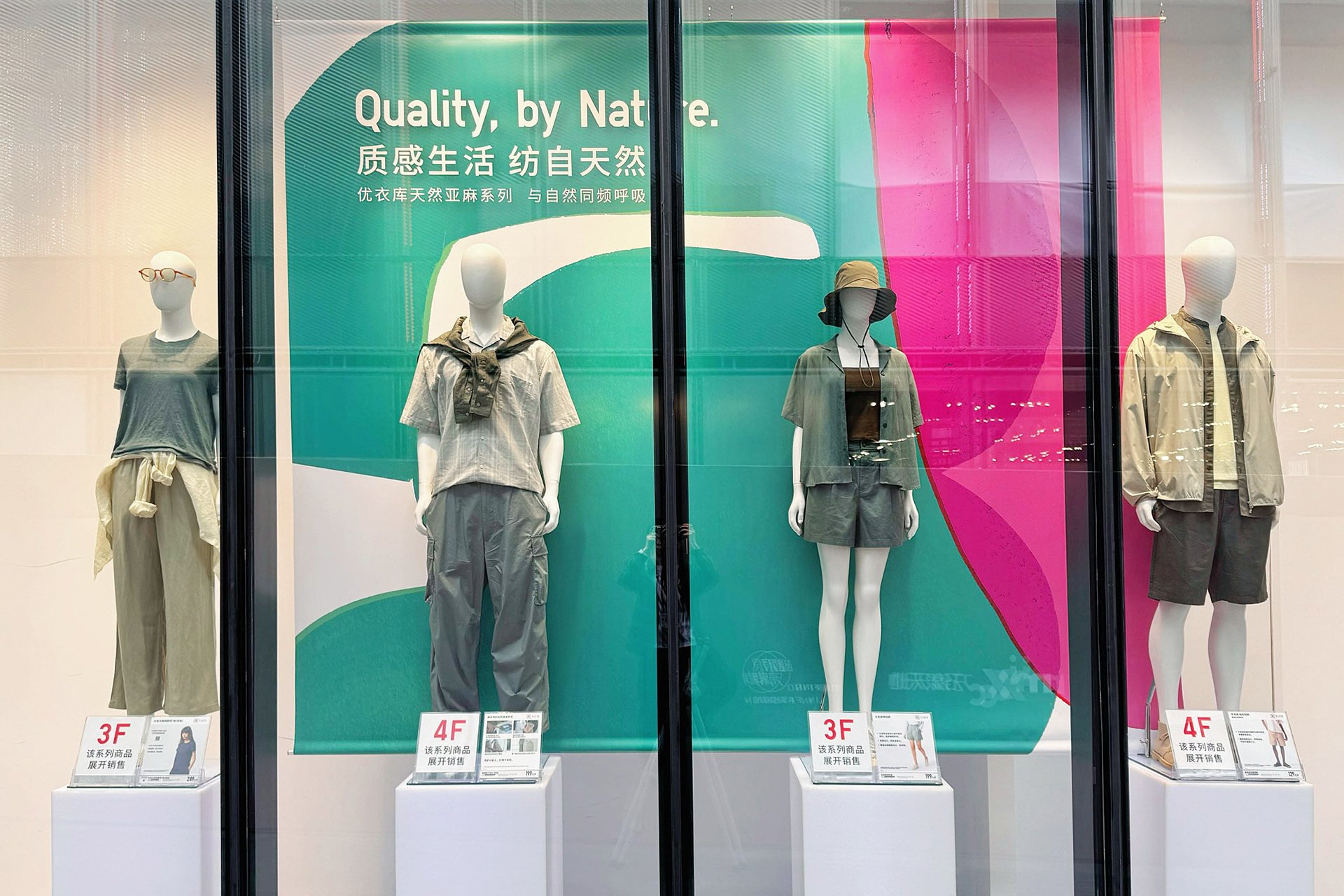 UNIQLO中国店舗のウィンドウディスプレイ。グリーンとピンクのアートを背景にリネン素材の春夏コーディネートを展示(アートワーク:サトウアサミ)UNIQLO China storefront window featuring green and pink abstract visuals with spring/summer linen outfits (Artwork by Asami Sato)