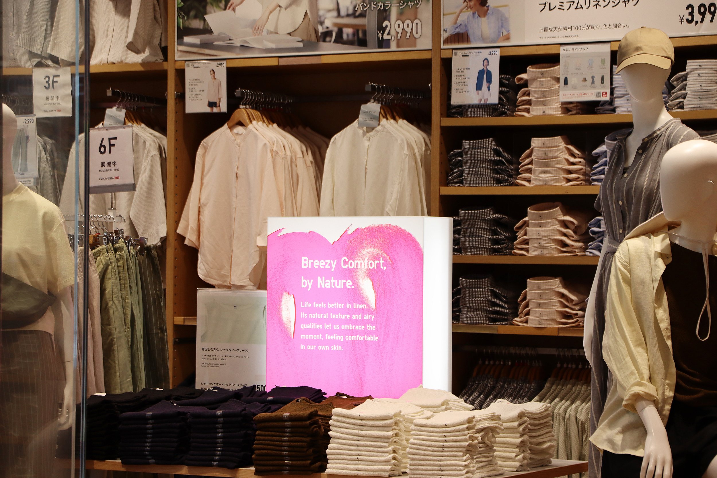 リネン素材の売場に設置された「Breezy Comfort, by Nature.」のメッセージとピンクアートライトパネル。Linen section at UNIQLO Ginza with light panel featuring pink brushstroke and “Breezy Comfort, by Nature.” campaign message from 2025 S/S visuals.