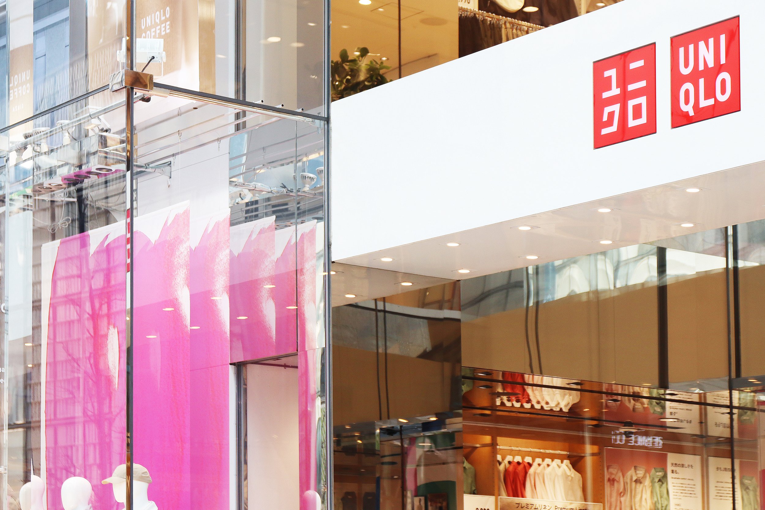 ユニクロ銀座店のエントランスを彩るピンクのブラッシュアートとロゴ。2025年春夏ビジュアルより。Close-up of UNIQLO Ginza entrance with vibrant pink brushstroke artwork and brand logo – part of 2025 Spring/Summer visuals by Asami Sato.
