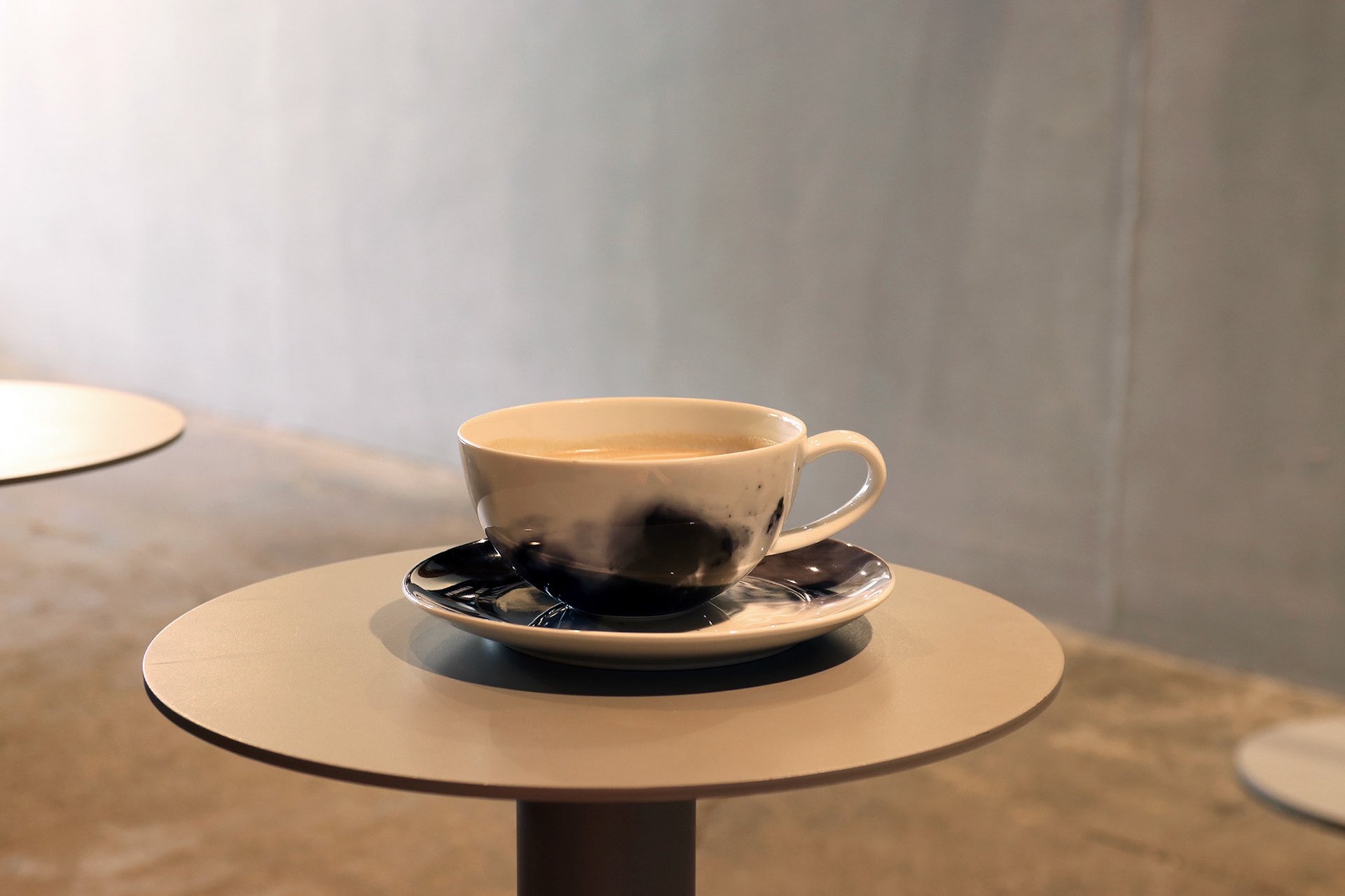 マーブル模様のカップとソーサーに注がれたコーヒー。グレーのラウンドテーブルの上で、静かな時間を演出。
A cup of coffee in a marble-patterned ceramic cup and saucer, placed on a gray round table—capturing a tranquil café moment.
