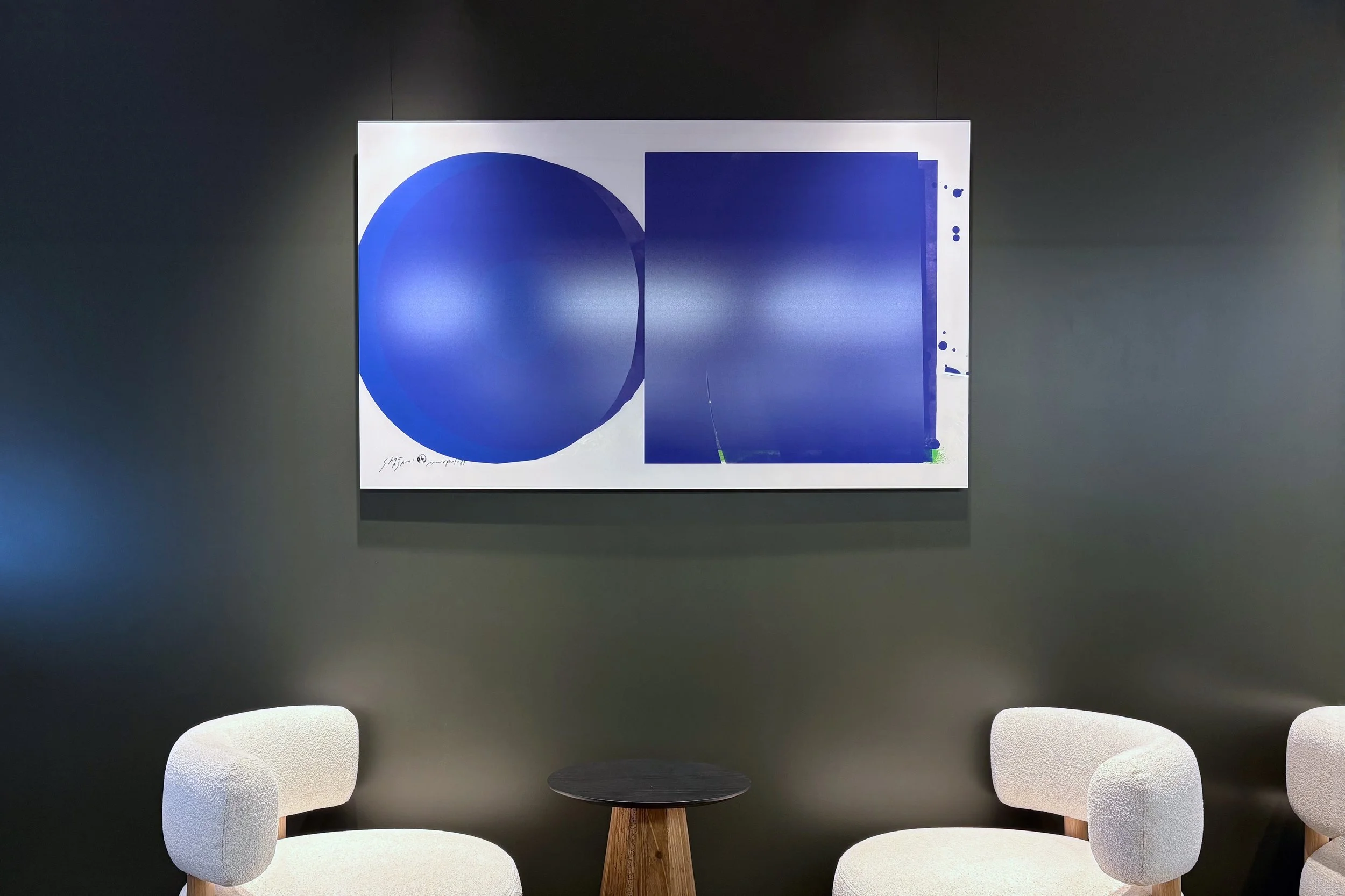 サトウアサミ（SATO ASAMI）によるオフィスアートの施工例。静かなグレーの空間に、円と四角が重なり合う青いグラフィックが知的なアクセントを添えています。