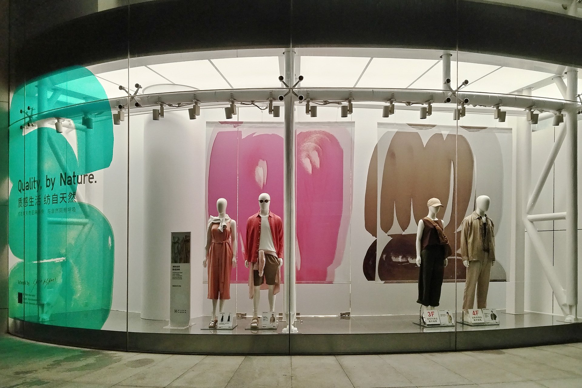 中国のUNIQLO店舗にて展示された、サトウアサミによる抽象アート(ピンク、ブラウン、グリーン)を背景にした2025年春夏ディスプレイ。UNIQLO store in China showcasing 2025 Spring/Summer display with abstract brushstroke art in pink, brown, and green by Asami Sato