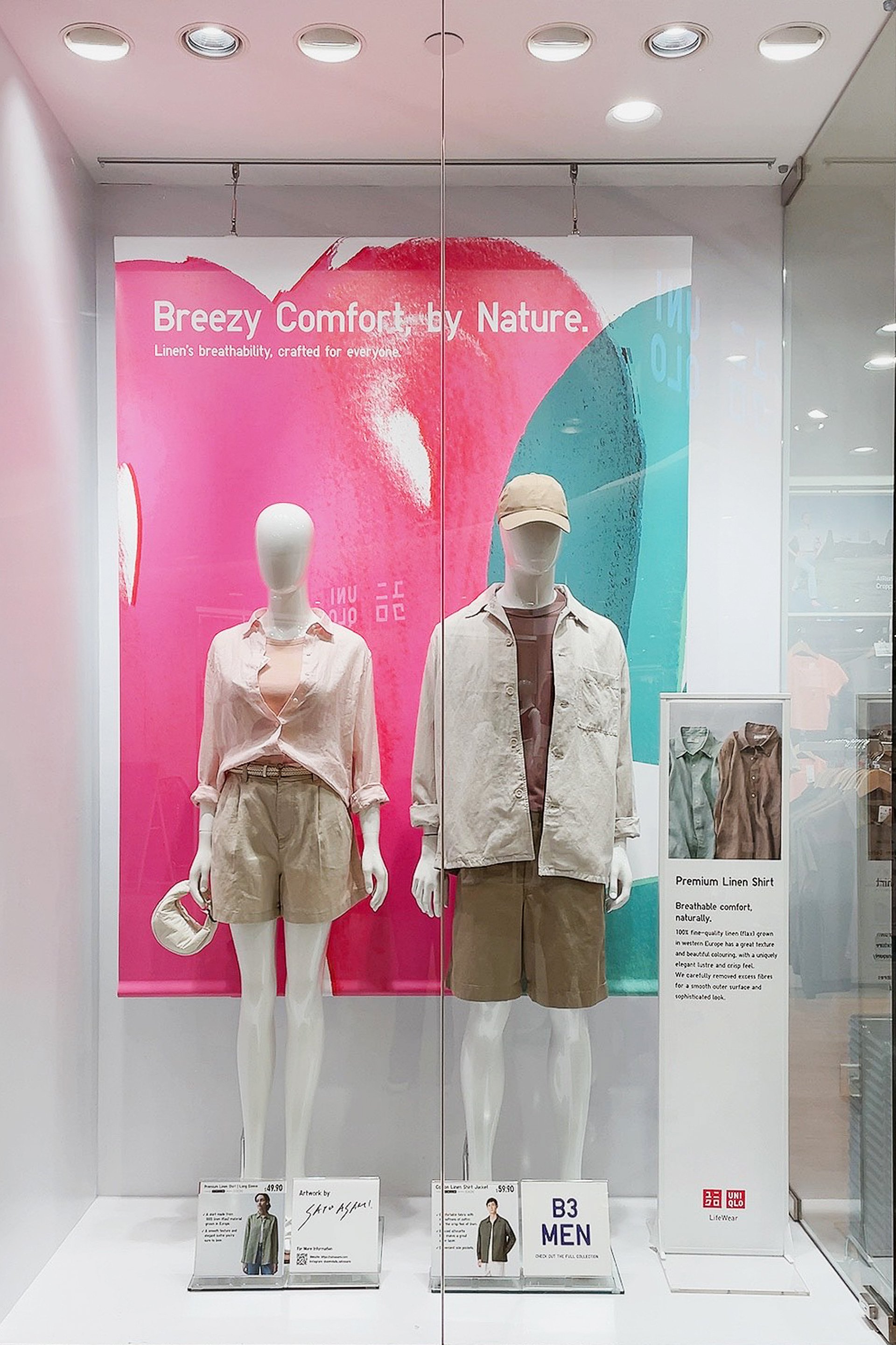 シンガポールのUNIQLO店内ディスプレイ。ピンクとグリーンのアートを背景にしたリネンシャツスタイル。In-store UNIQLO Singapore display featuring linen shirts with pink and green abstract art backdrop by Asami Sato