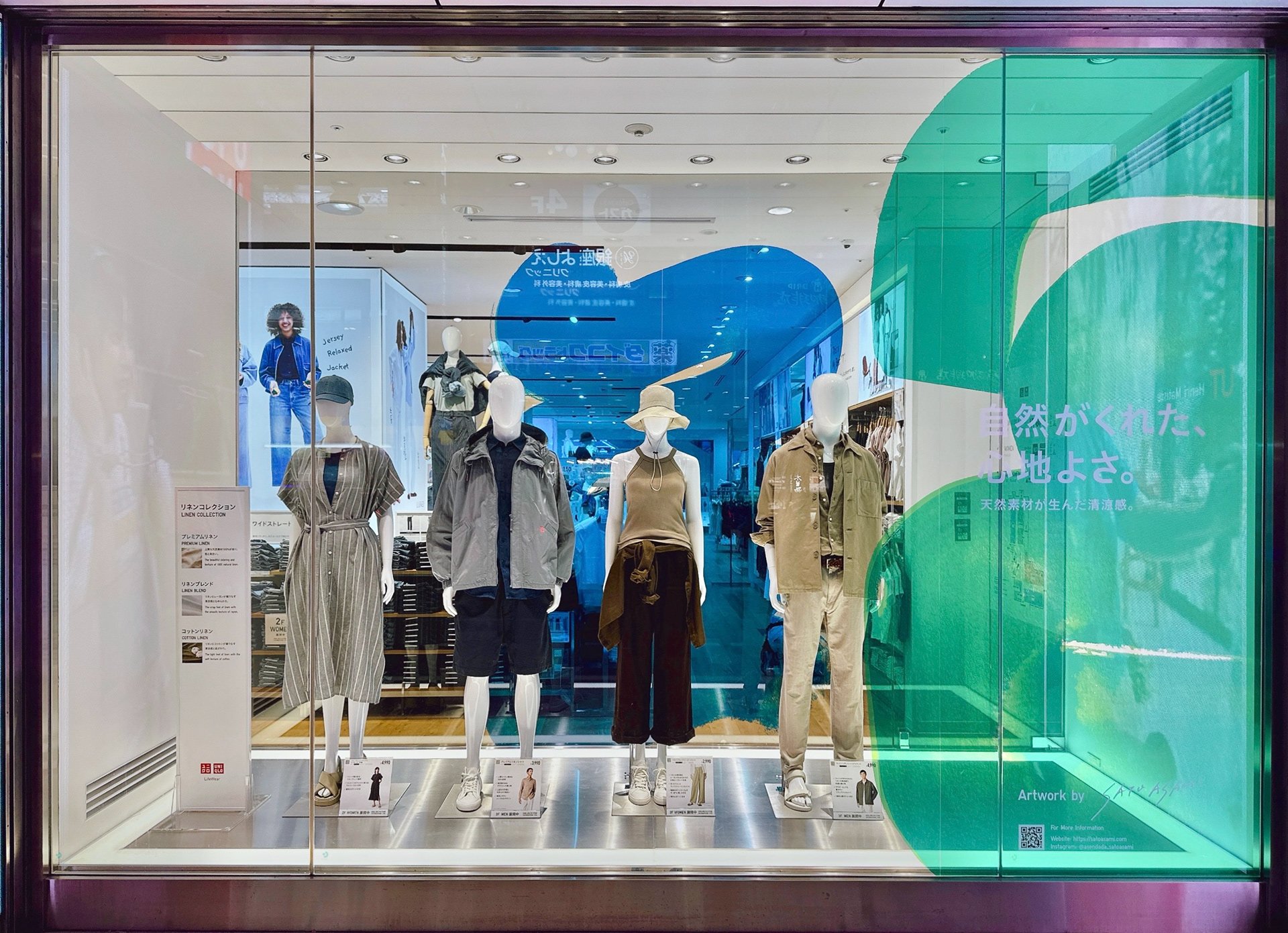 ユニクロ店舗ウィンドウに展開された、グリーンとブルーの抽象的アートワークと春夏リネンコレクション(アートワーク:サトウアサミ)UNIQLO storefront display featuring green and blue abstract artwork with Spring/Summer linen collection outfits (Artwork by Asami Sato)