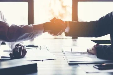 Two people shaking hands across a conference table in a business meeting