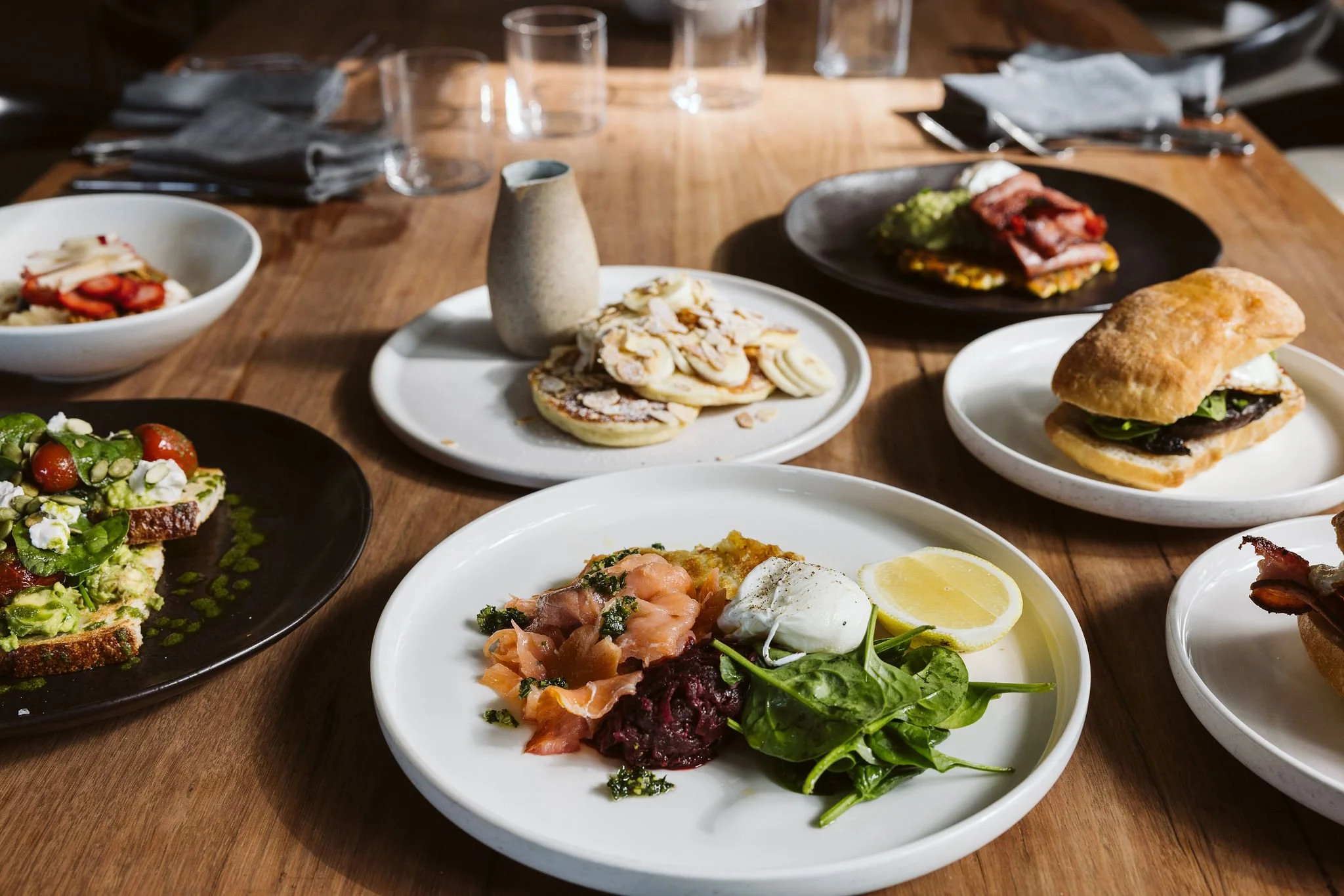 Slices of toasted bread topped with guacamole, cherry tomatoes, ricotta cheese, fresh basil, and pumpkin seeds, drizzled with green sauce.