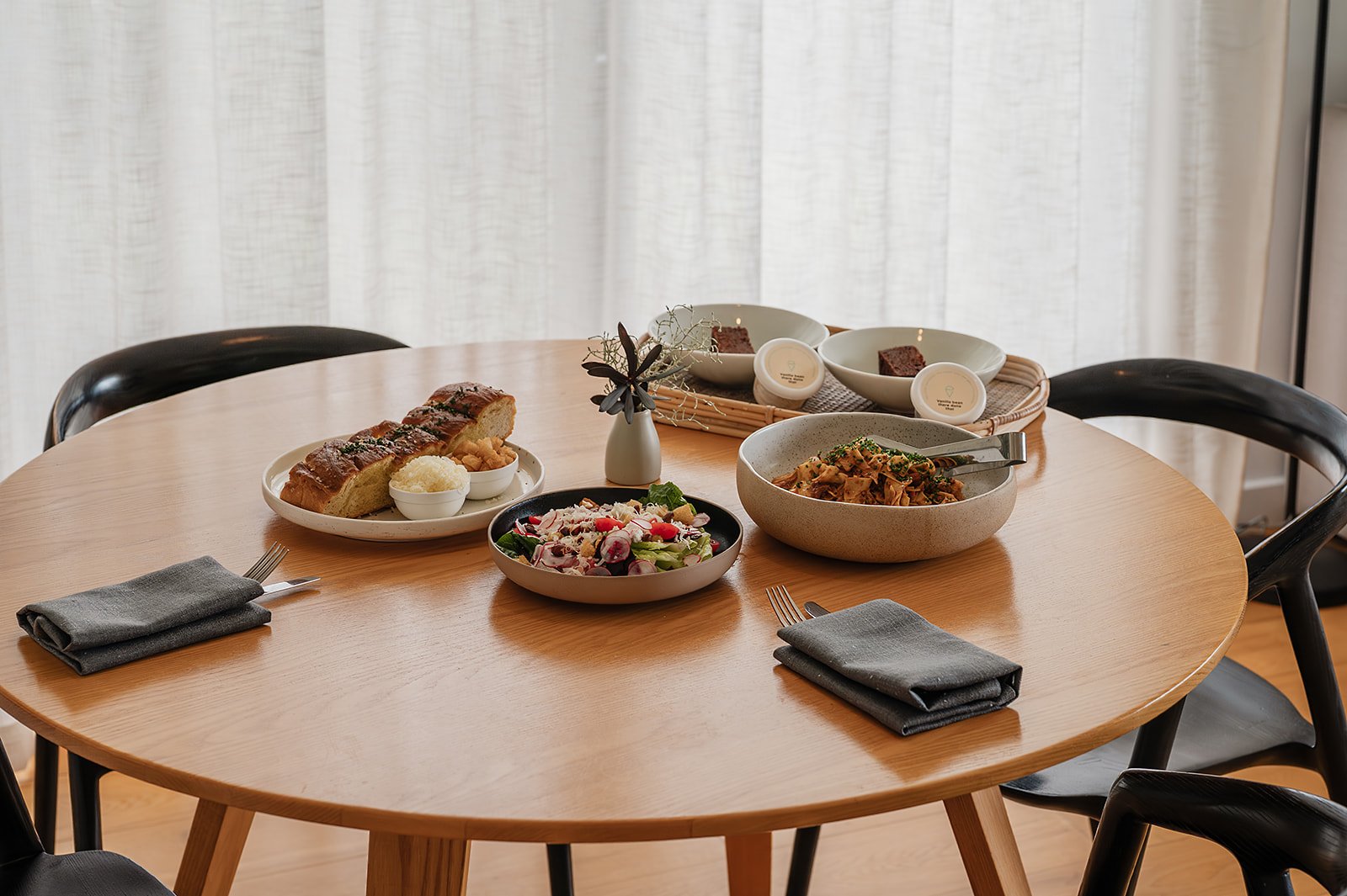 Three plates of food on a white table, including a dessert with cherries and pine nuts, a plate with fish, and another plate with baked vegetables and rice. There is a menu or informational paper on the table.
