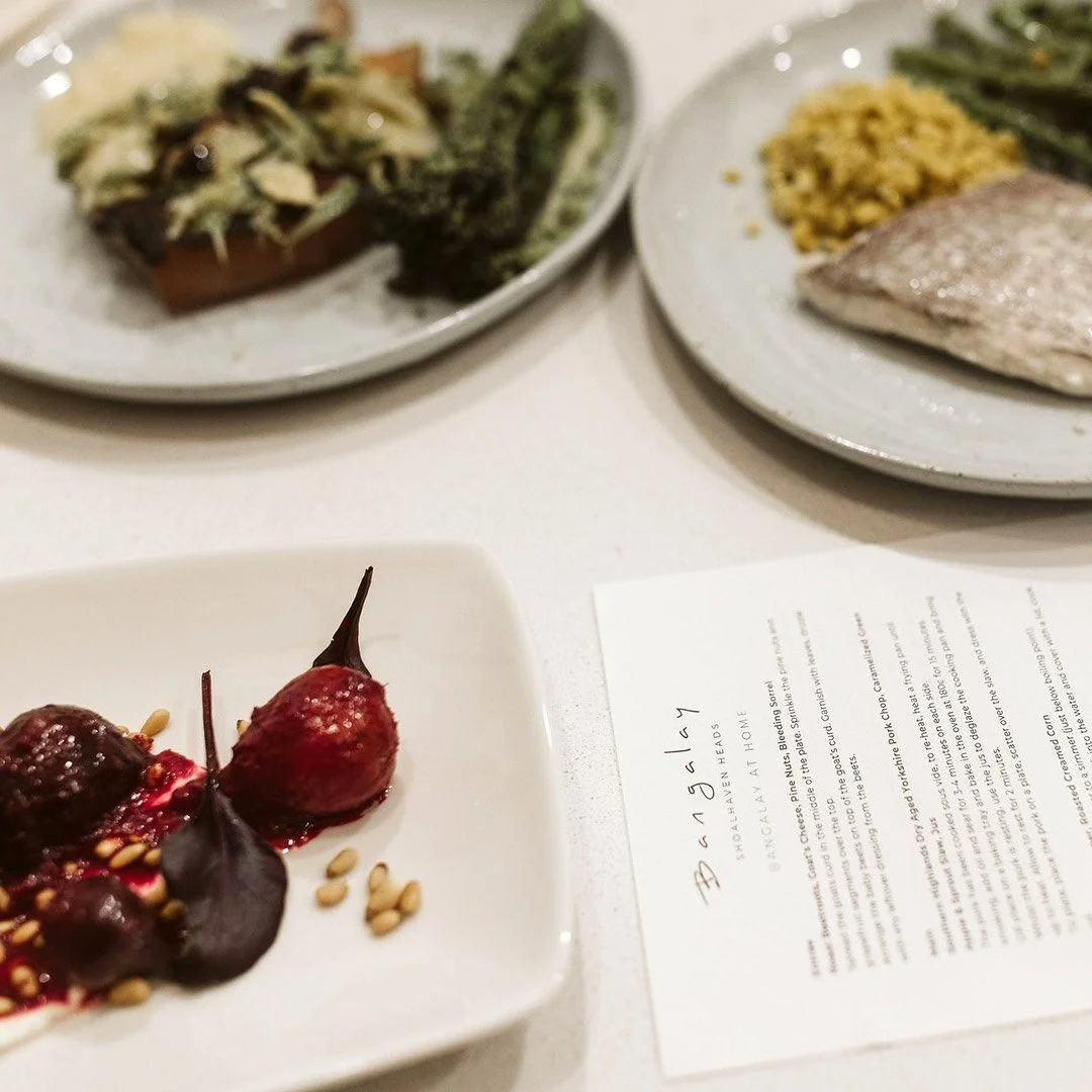 Three dinner plates and a dessert plate on a white table. The dessert plate has a red cherry with some sauce and pine nuts. The plates contain fish, rice, and vegetables. A paper with text is also on the table.