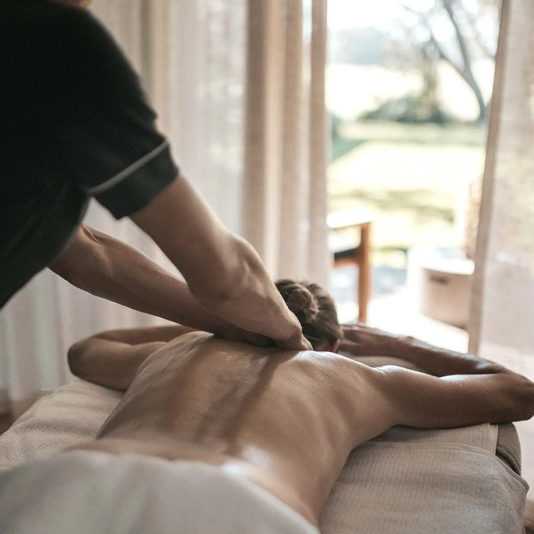 Person giving a back massage to a person lying face down on a massage table in a well-lit room.