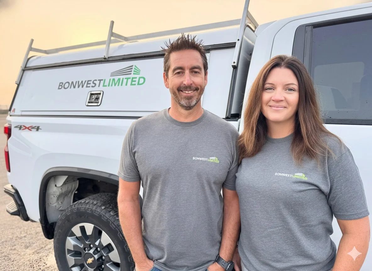 Two people wearing gray shirts with 'Bonwest Limited' posing in front of a white pickup truck with a ladder on top, at sunset.