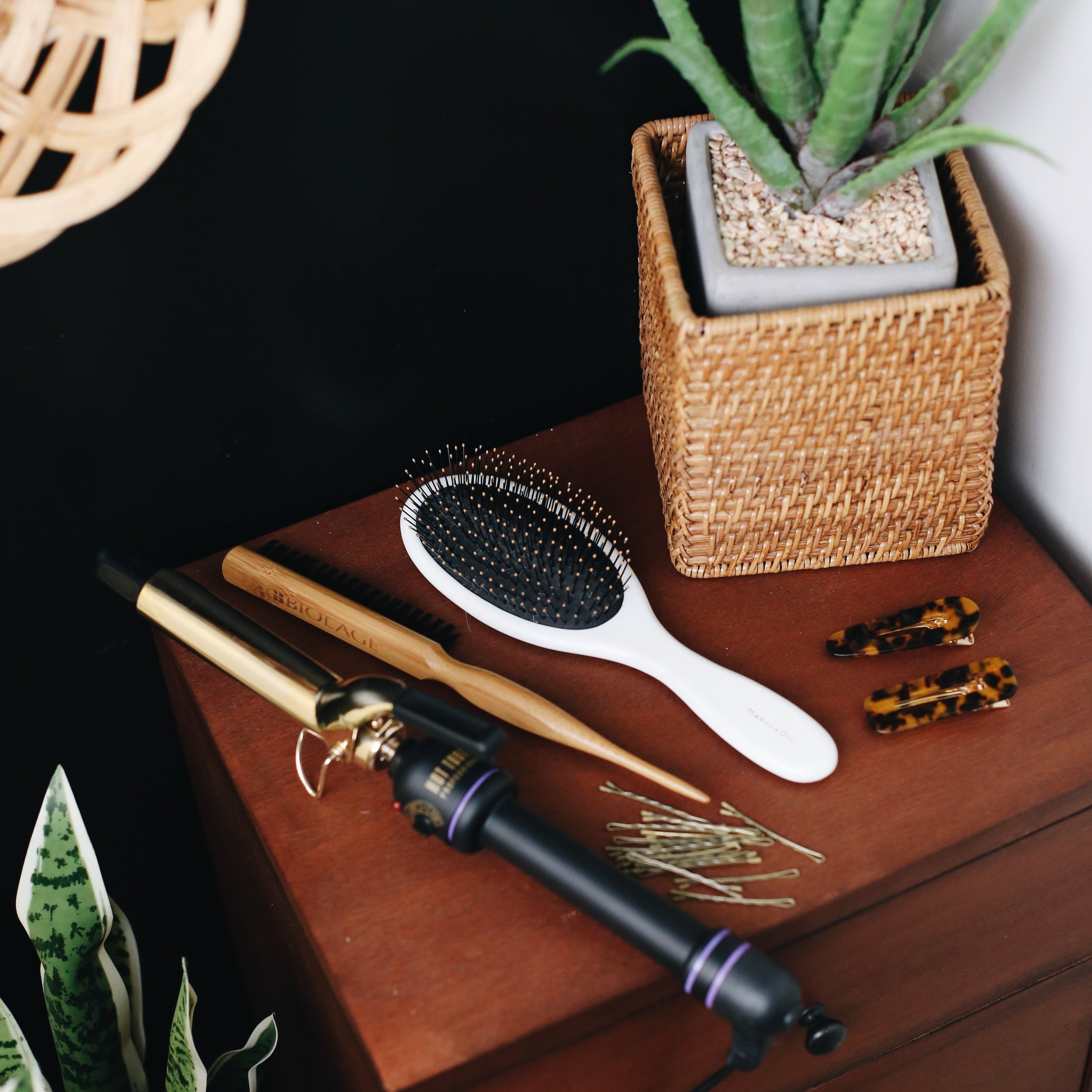 A black hairbrush with gold accents, a black and purple flashlight, a black hair clip, a string of gold bobby pins, and tortoiseshell hair clips on a wooden surface.