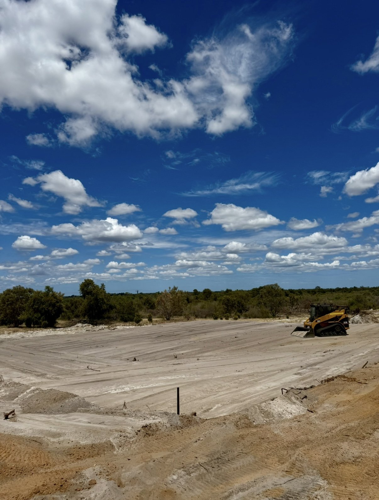 A Caterpillar skidsteer working on a dirt pathway in a backyard, surrounded by trees and a fence.