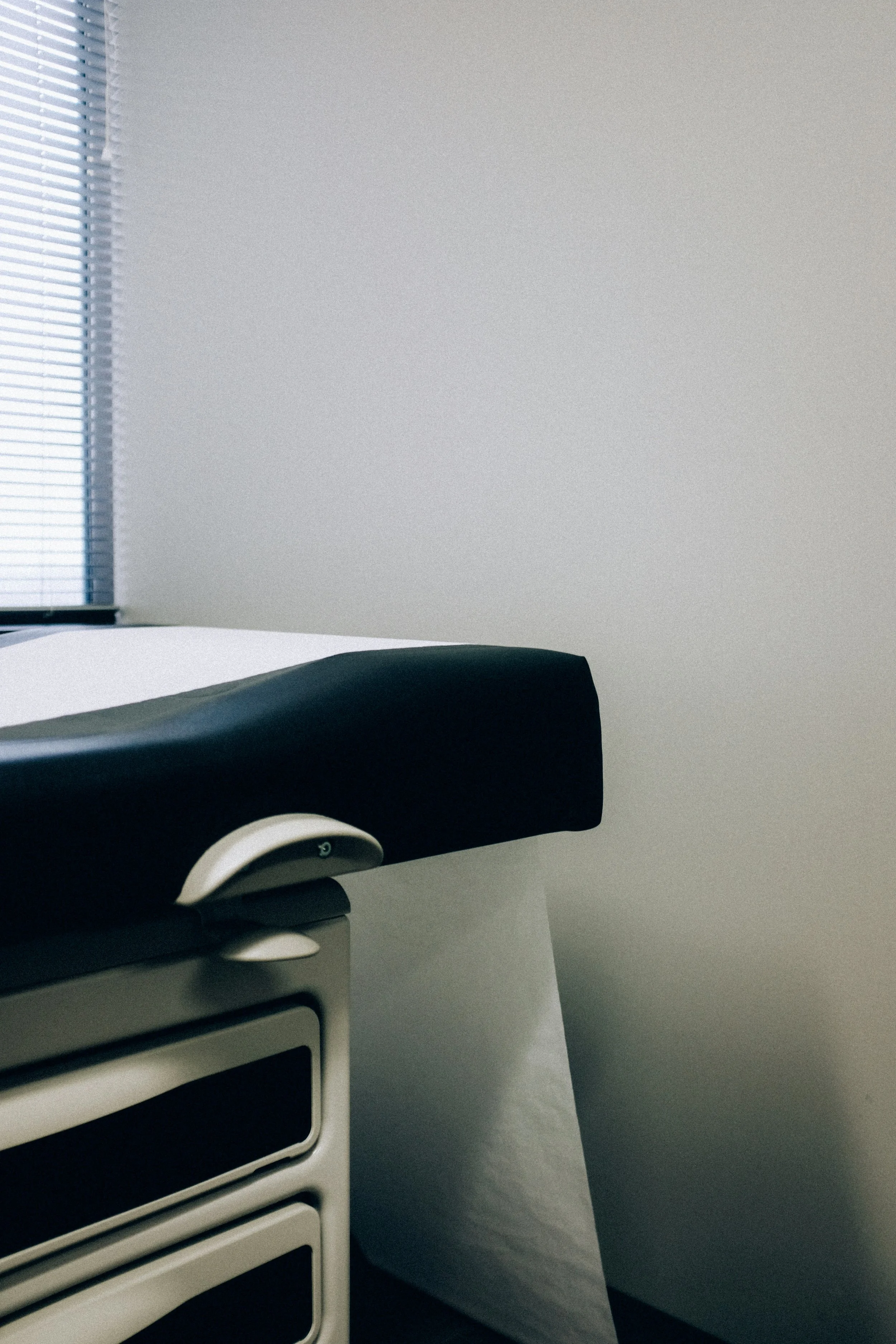 Close-up of a hospital examination table with an adjustable black cushion and a white wall in the background.