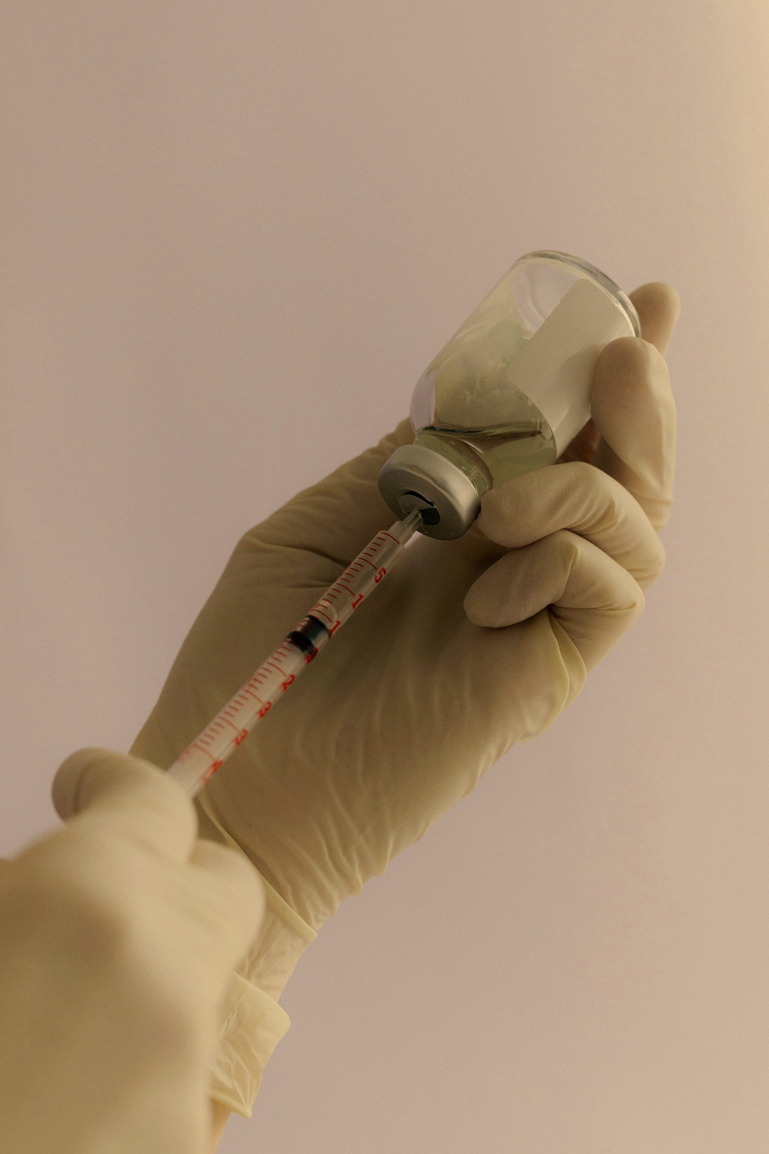 A healthcare professional's gloved hand holding a small glass vial and a syringe, preparing to administer a vaccine.