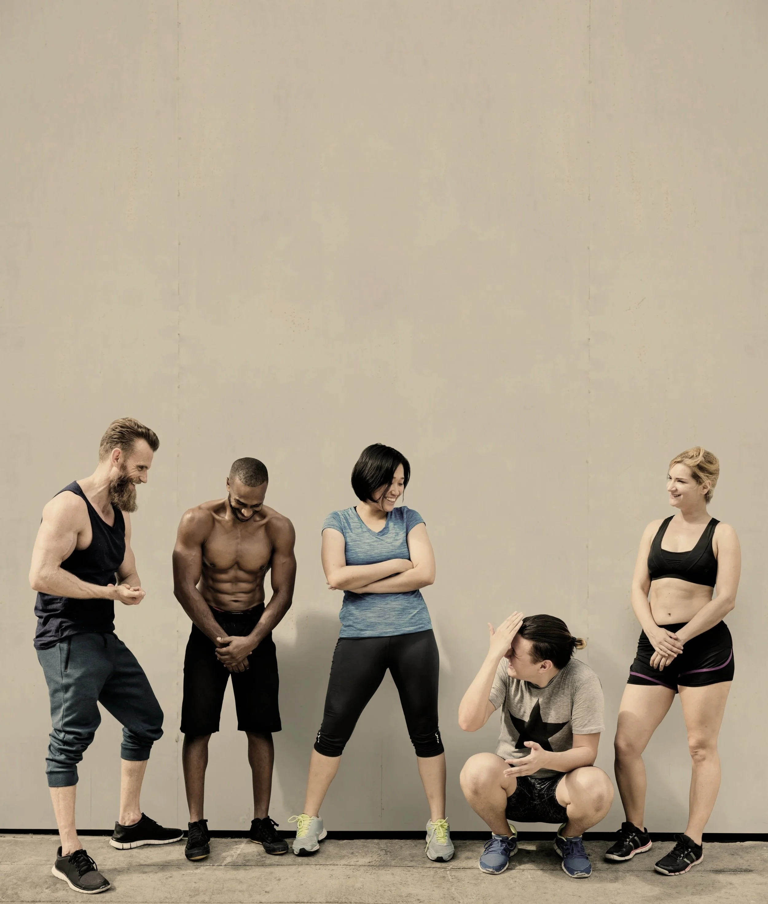 Group of five diverse people laughing and talking in workout clothes against a plain wall.