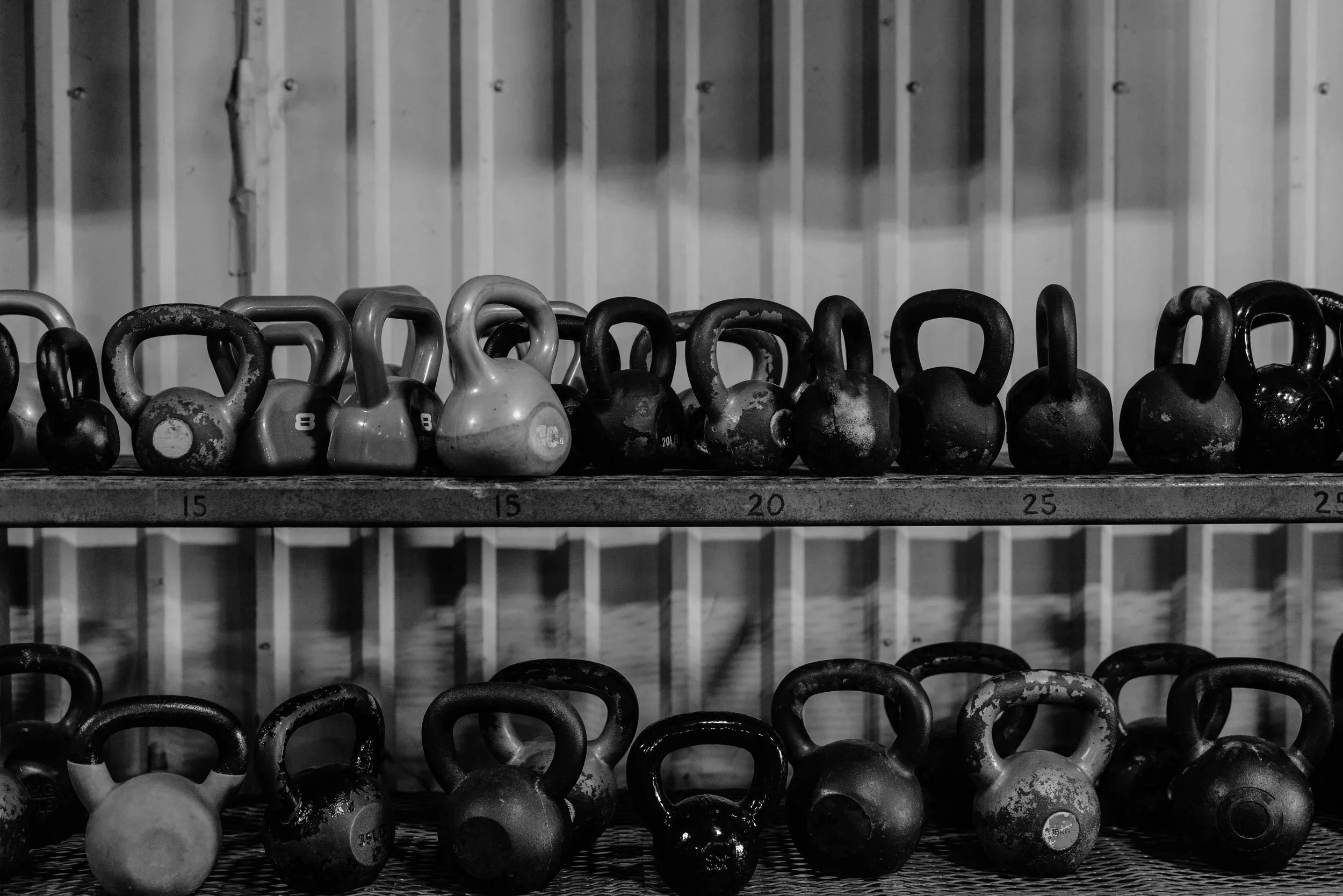 Black and white photo of kettlebells arranged on metal racks in a gym.
