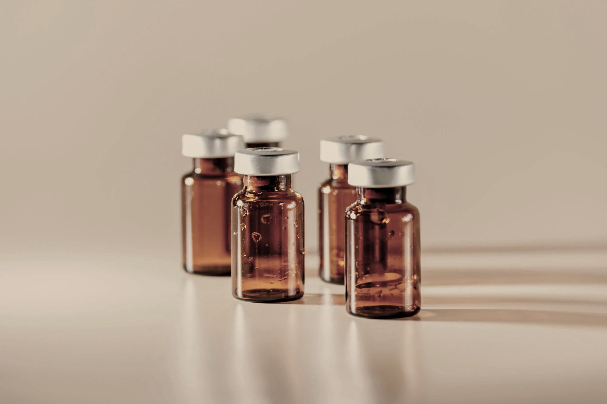 Six brown glass vials with silver caps arranged on a light surface, casting shadows.