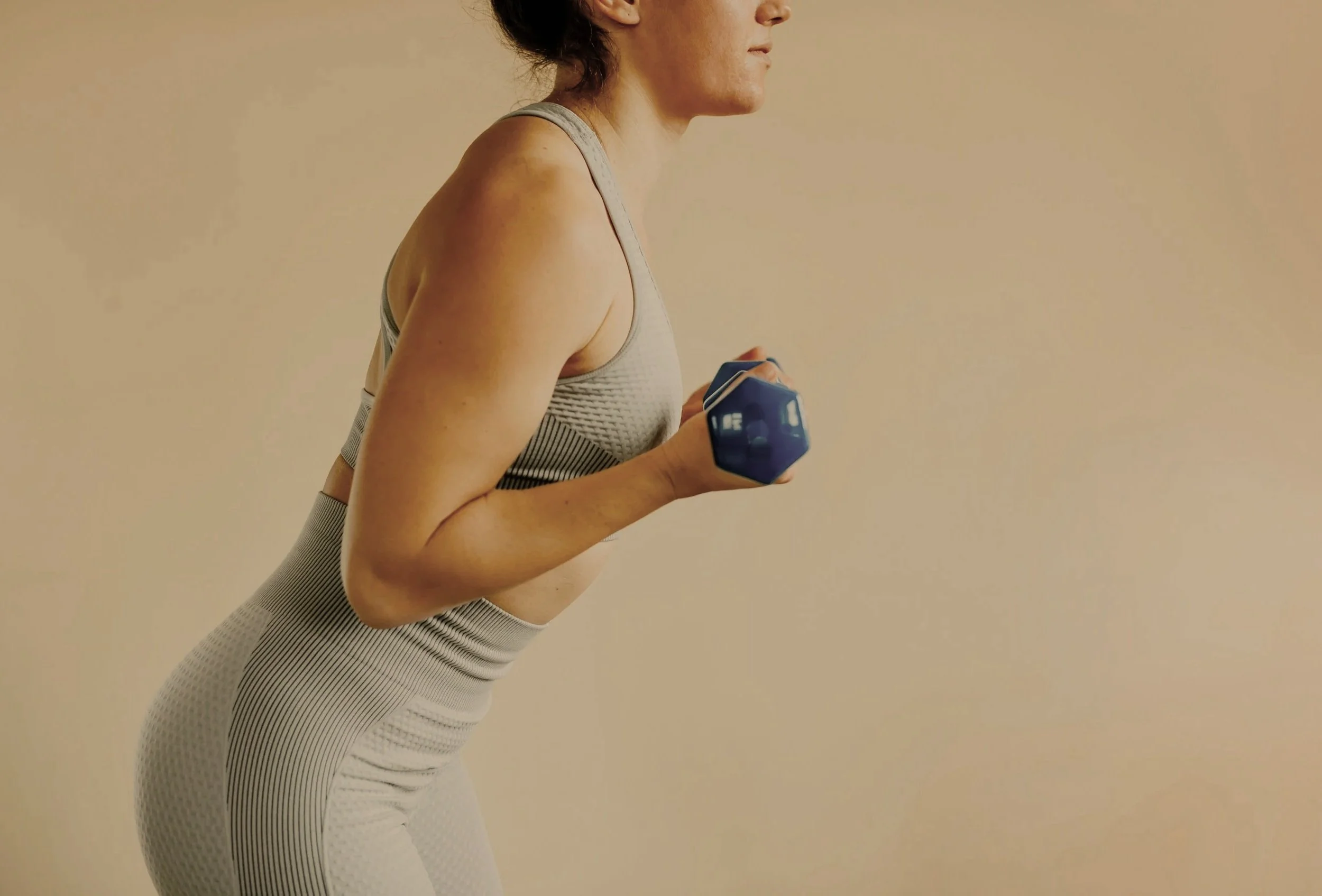 A woman in workout clothes holding a blue dumbbell, engaging in strength training.