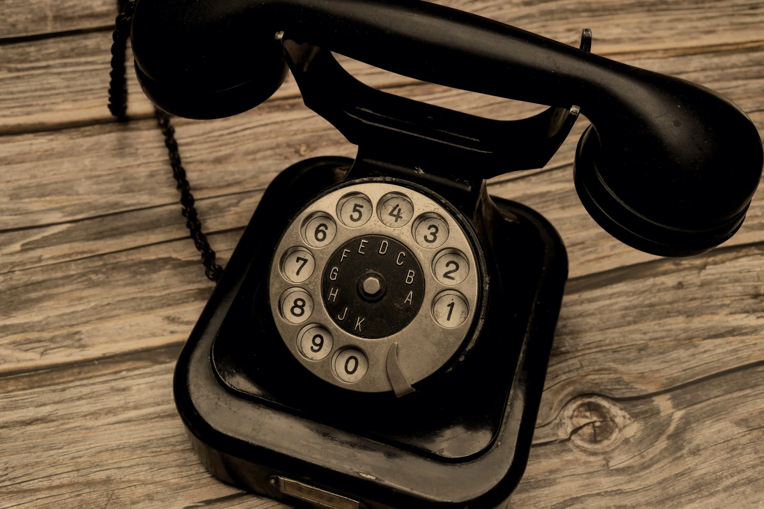 An old black rotary telephone on a wooden surface.