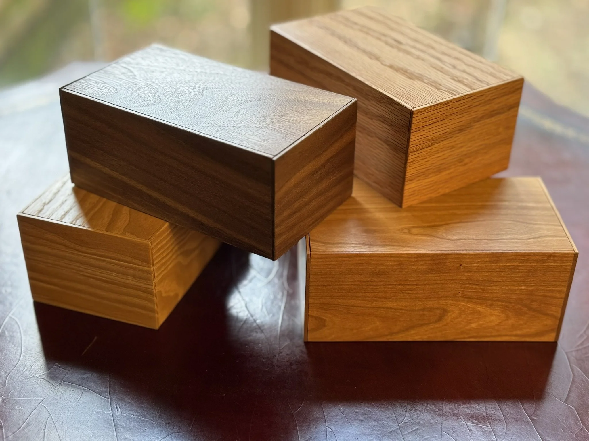 Five wooden boxes of different materials stacked on a surface near a window.
