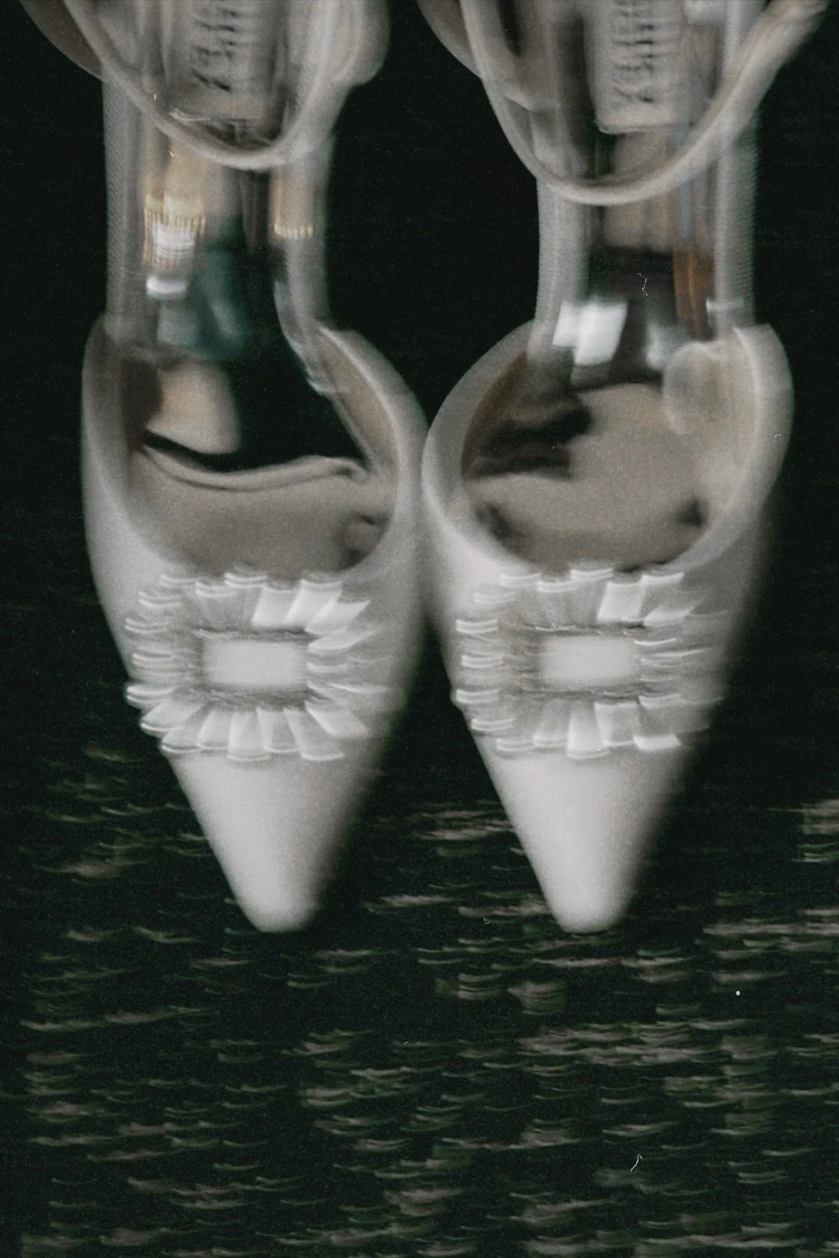 A pair of shiny, pointed-toe high-heeled shoes with decorative elements on the front, placed on a reflective black surface.