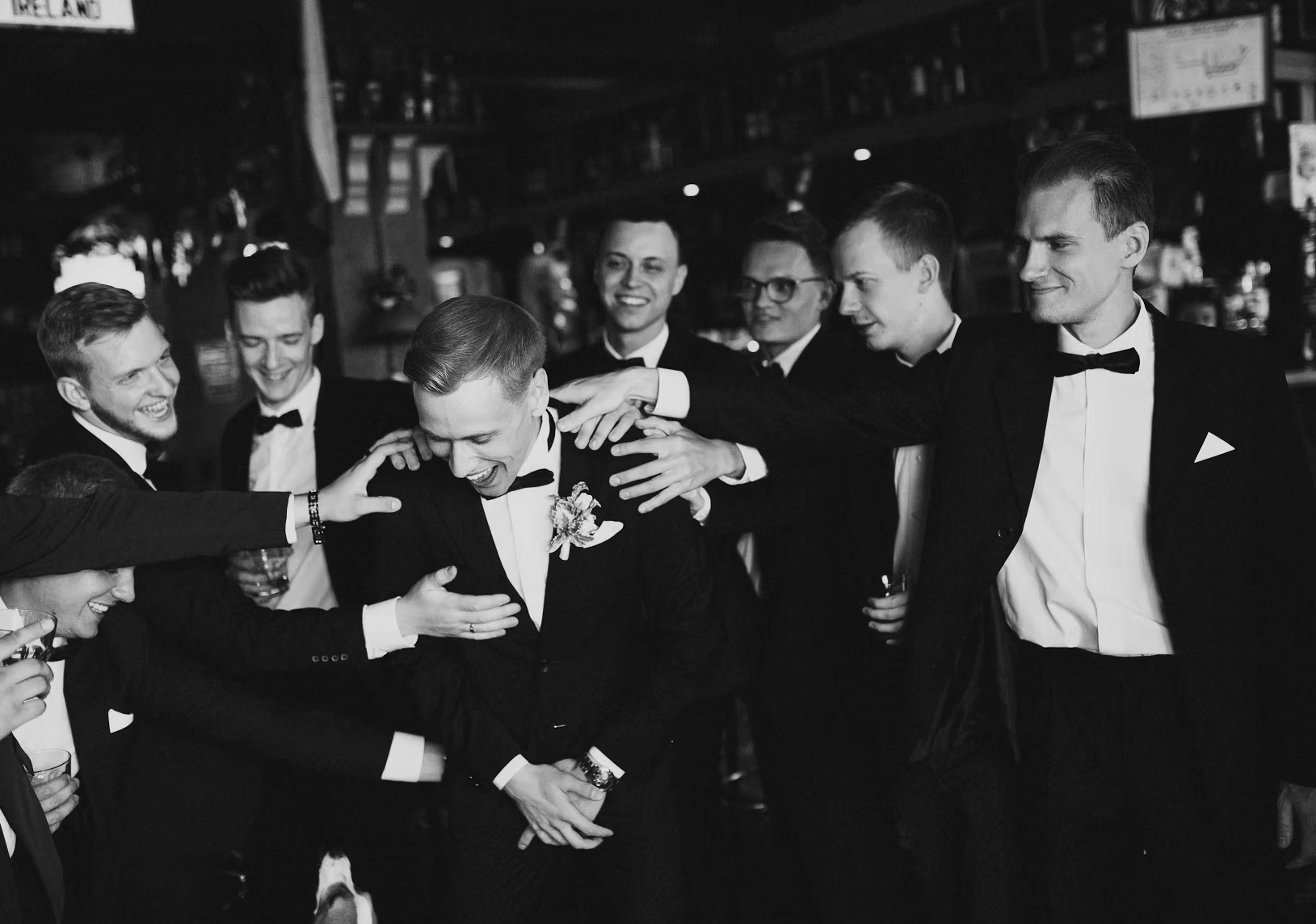 A group of men in tuxedos celebrating and laughing at a party or wedding reception.
