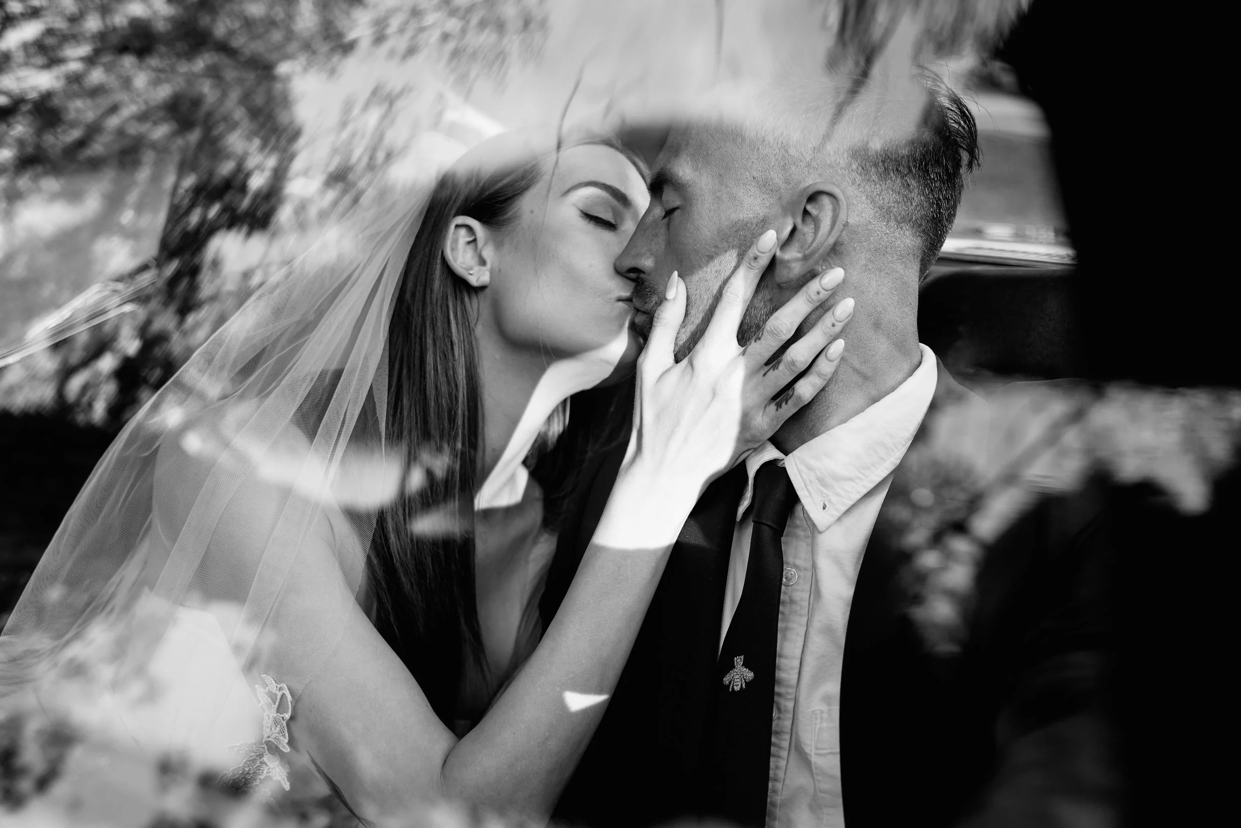 A black and white photograph of a bride and groom sharing a kiss under a veil.