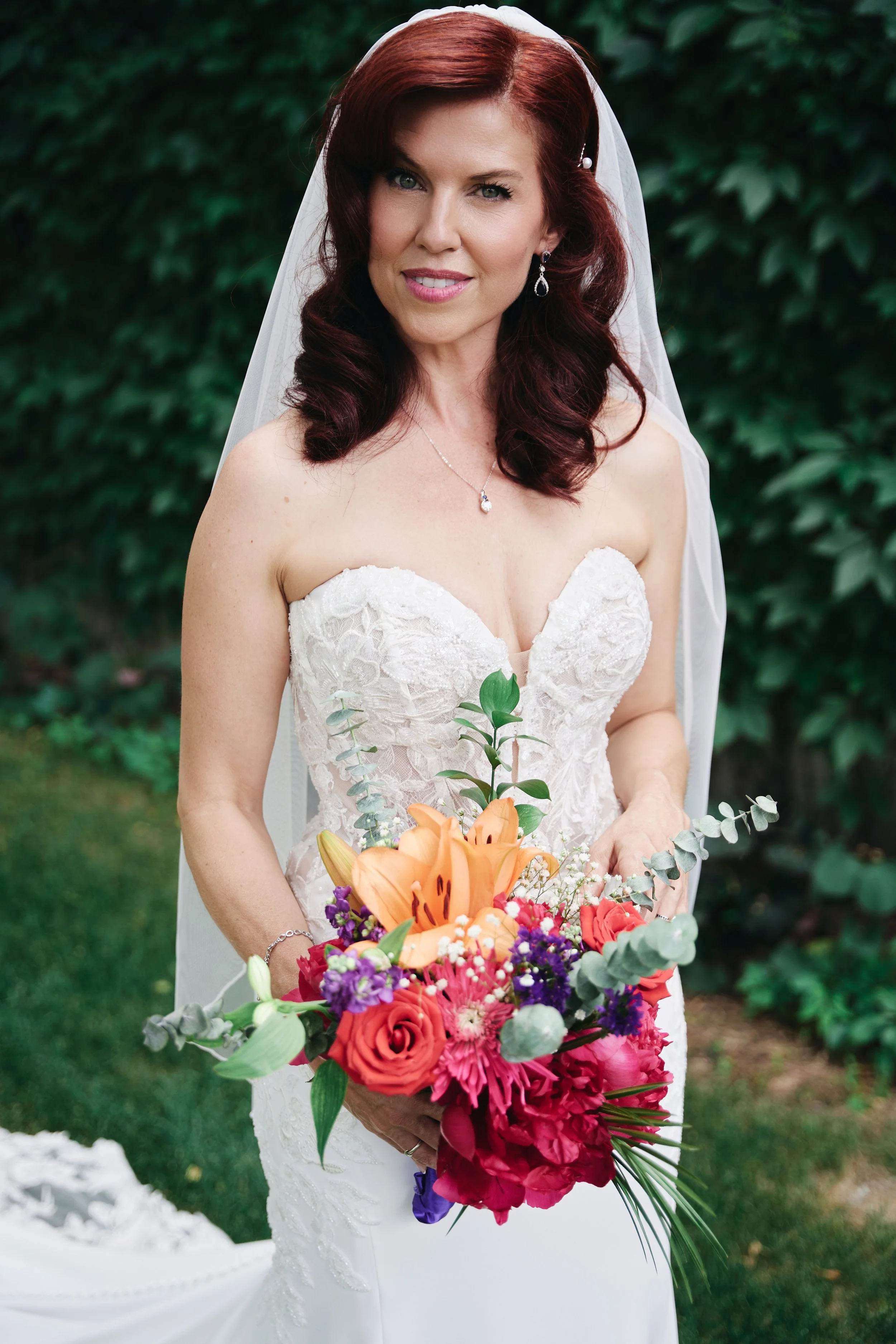 A woman with dark red hair in a wedding dress holding a colorful bouquet of flowers.