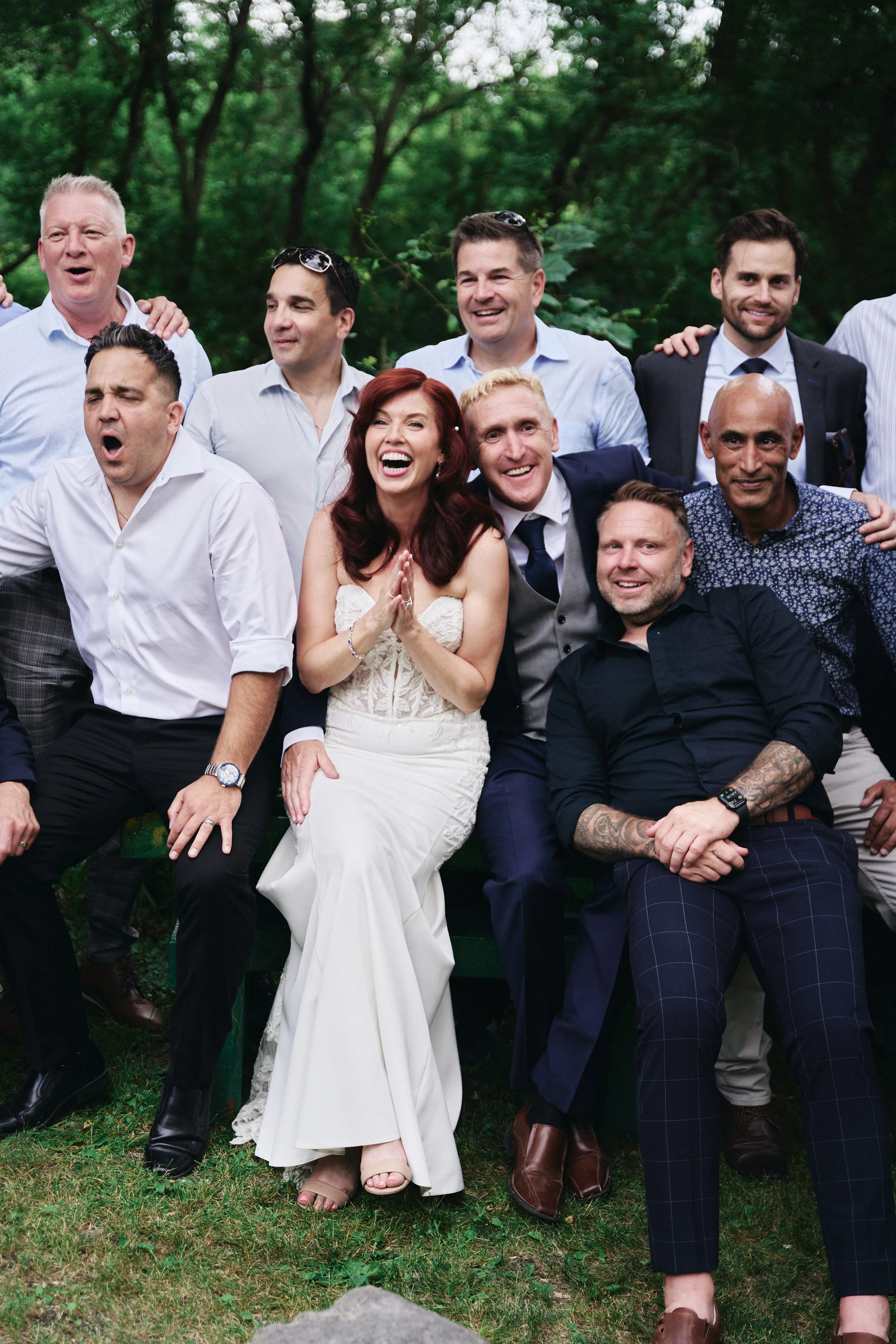 Group of people smiling and celebrating outdoors in a park, with trees in the background.