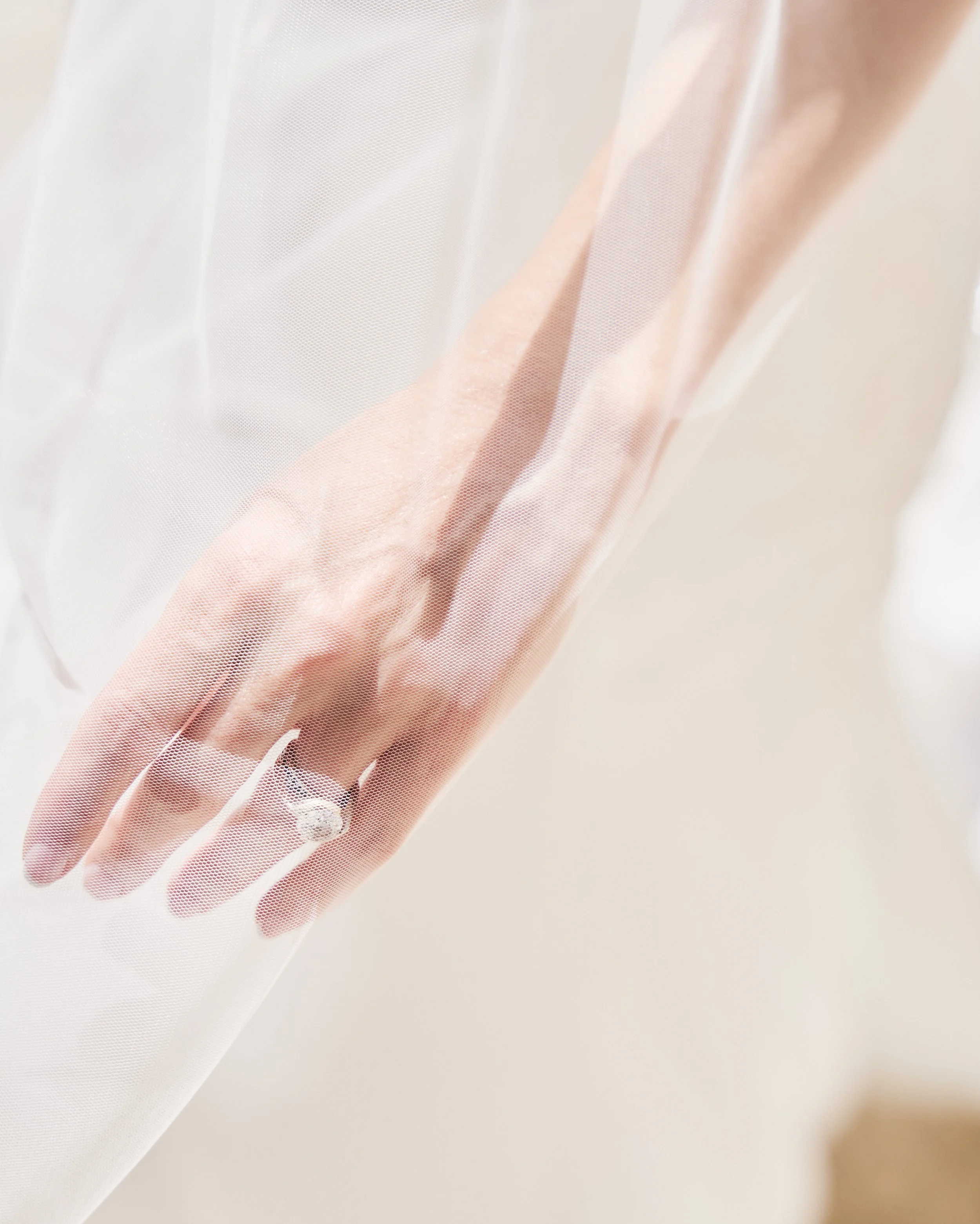 Close-up of a hand with a wedding ring, rest on a sheer fabric surface.