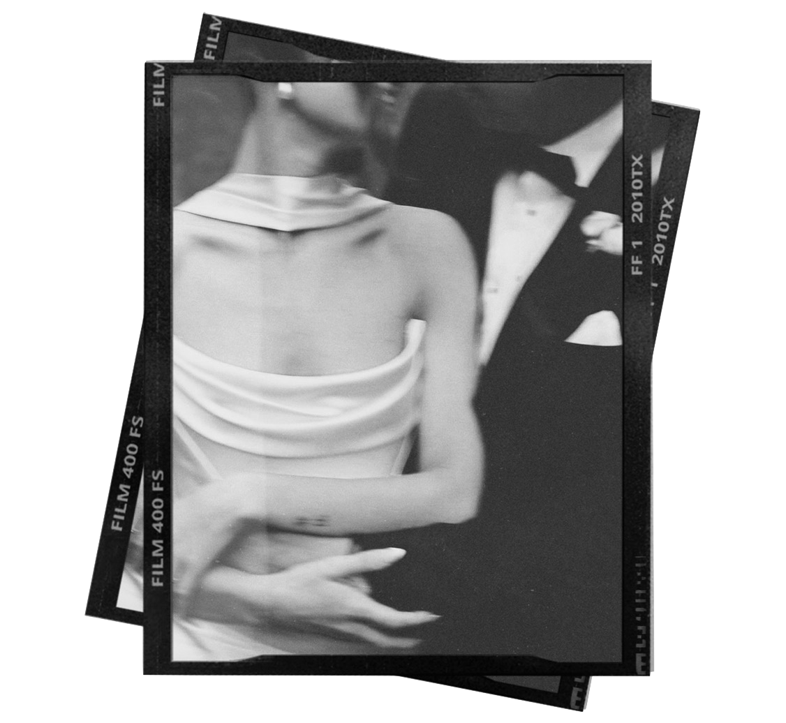 Black and white photo of a woman in a satin dress, with another person dressed in a tuxedo nearby, in an artful, candid style.