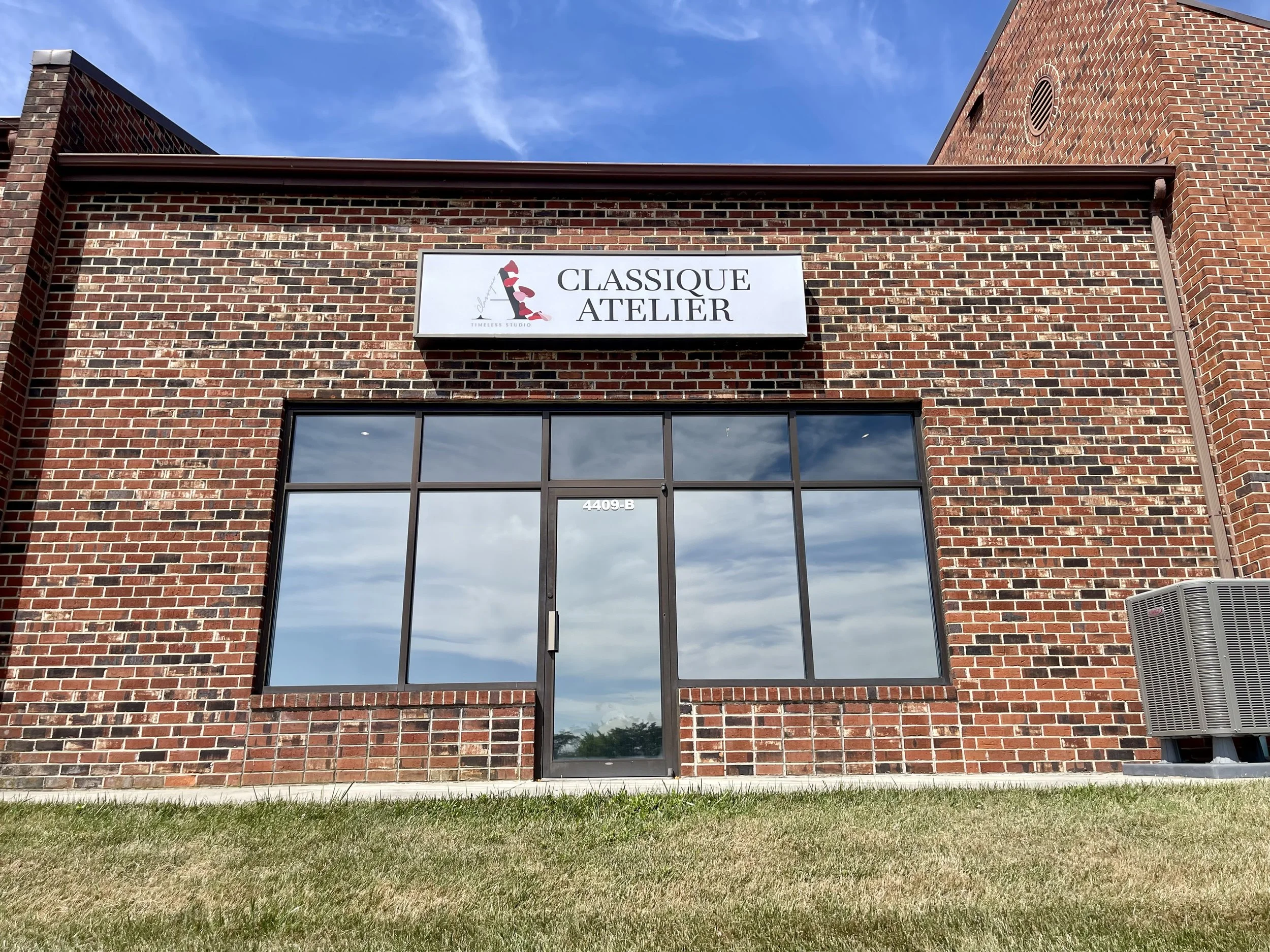 Brick building with large glass windows and a sign that reads 'Classique Atelier' above the entrance.