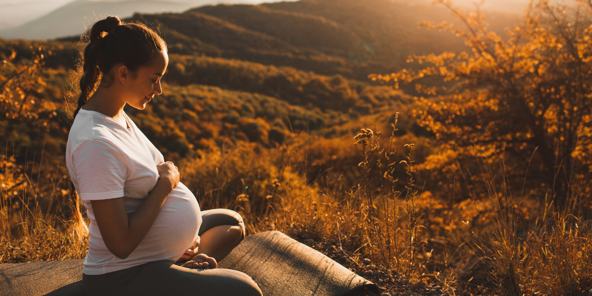 pregnant woman holding belly sitting on yoga mat in nature