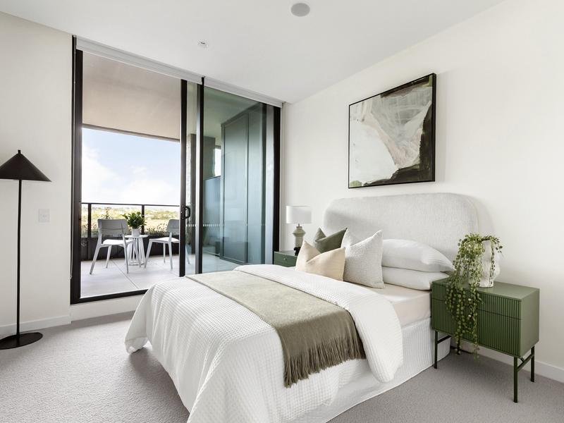 Modern bedroom with a white bed, green side tables, and balcony with outdoor seating