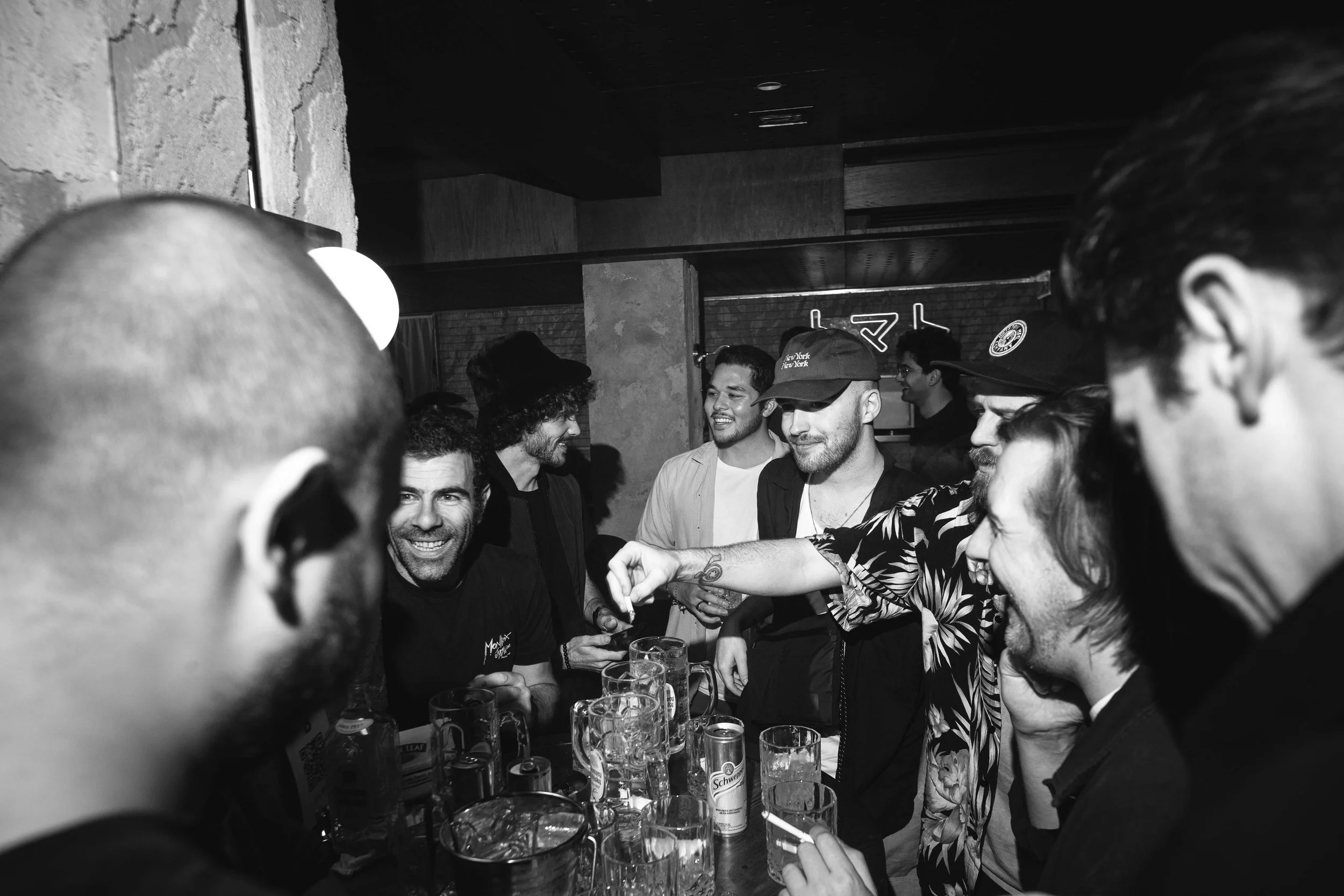 Group of people socializing and talking at a bar, some smiling and drinking, in a casual setting.