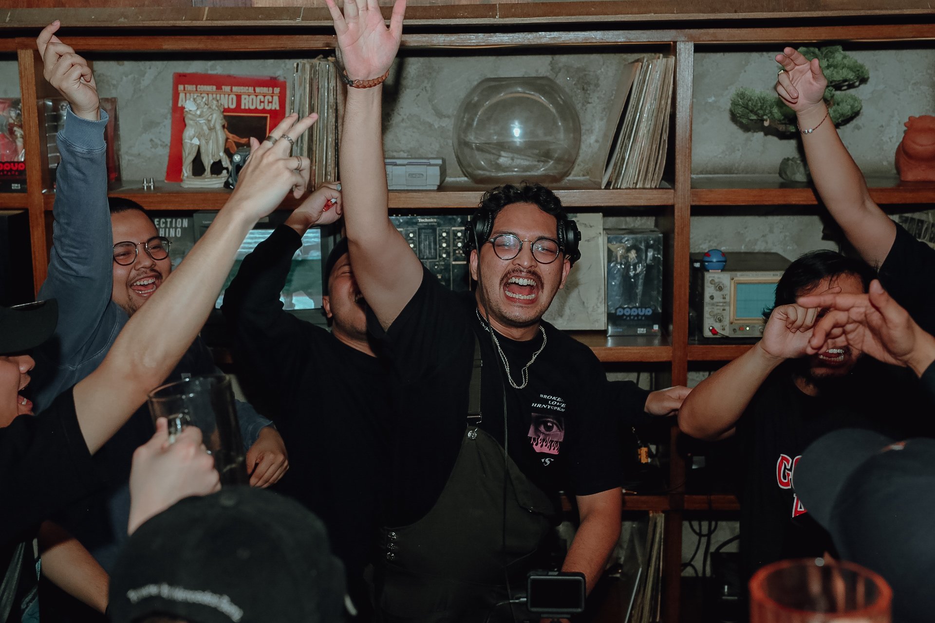 Group of people celebrating with raised hands in a room decorated with vintage records and shelves partying in Jakarta, Bebop, Senopati.