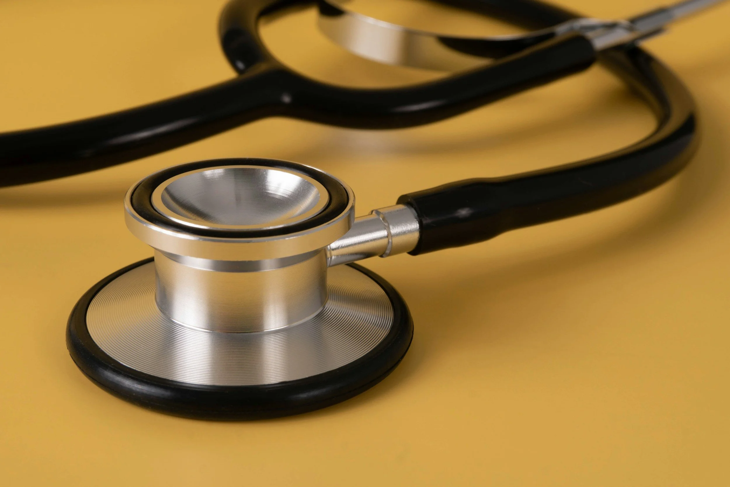 A close-up of a stethoscope with a silver chest piece and black tubing on a yellow background.