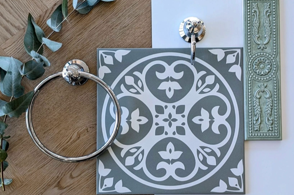 A decorative tile with a black and white intricate pattern, a round metal towel ring, and a glossy green tile with detailed carving on it.