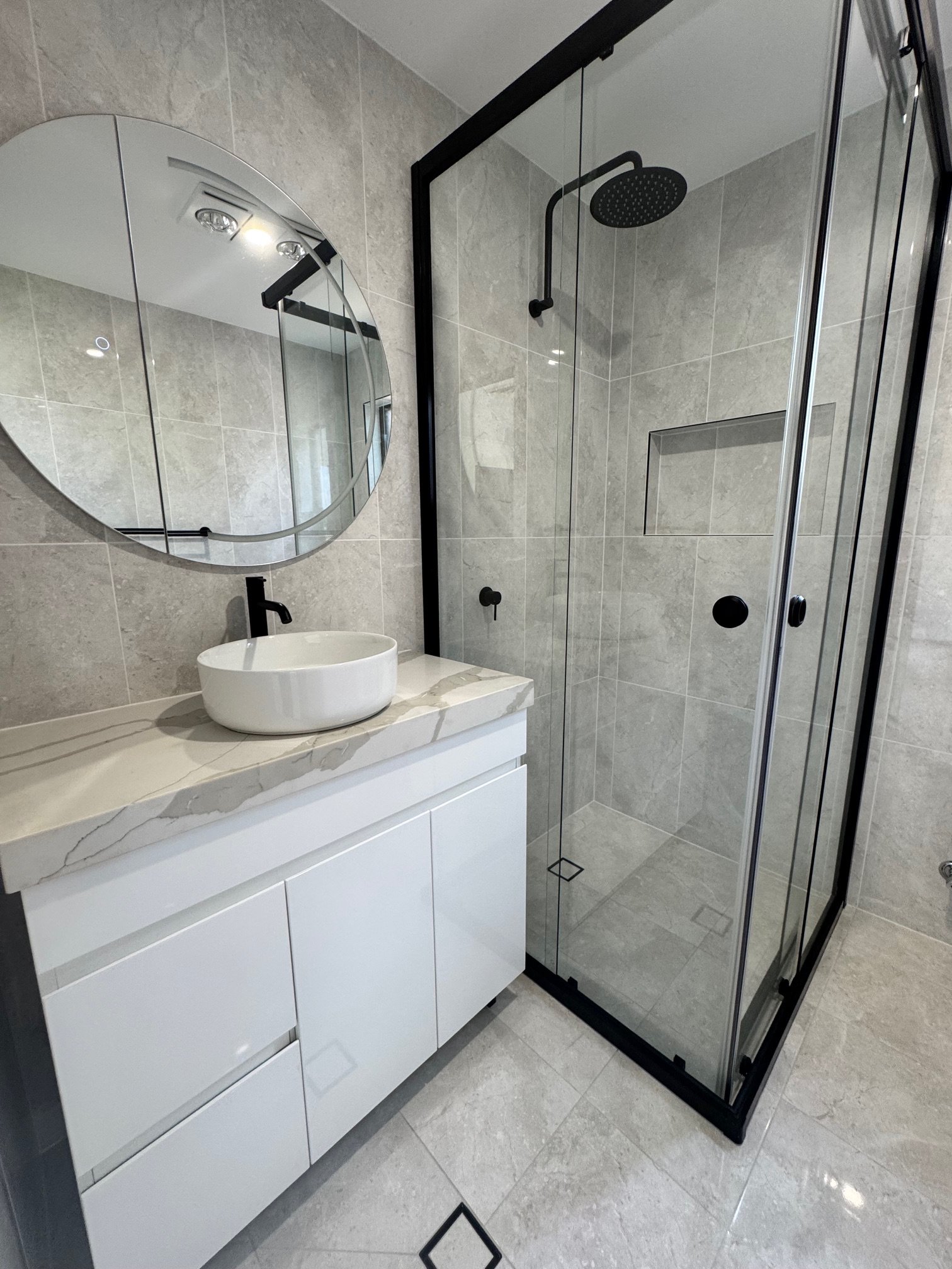 Modern bathroom featuring a floating vanity with a round vessel sink, a mirror, and a walk-in shower with glass door and black fixtures.