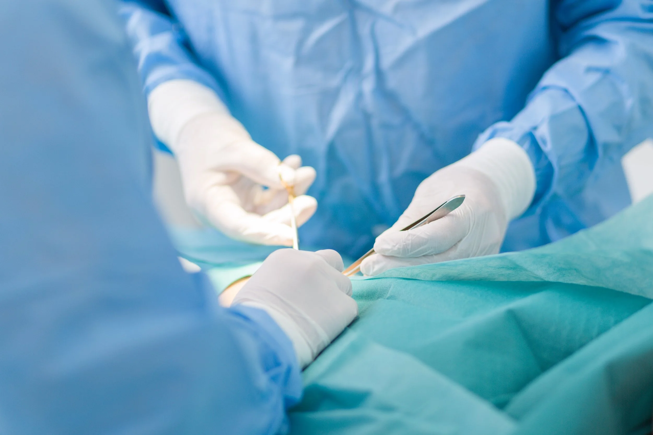 Close-up of surgeons’ gloved hands performing a procedure with surgical instruments in a sterile operating environment.