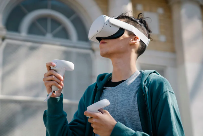 A young person wearing a virtual reality headset holding a game controller outdoors.