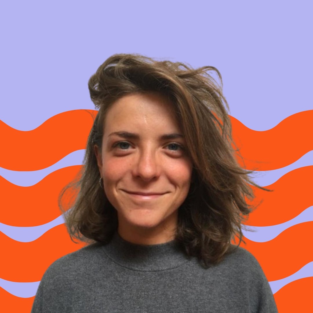 Close-up of a smiling woman with shoulder-length wavy hair, wearing a gray turtleneck sweater, against a background of orange wavy lines on a purple backdrop.