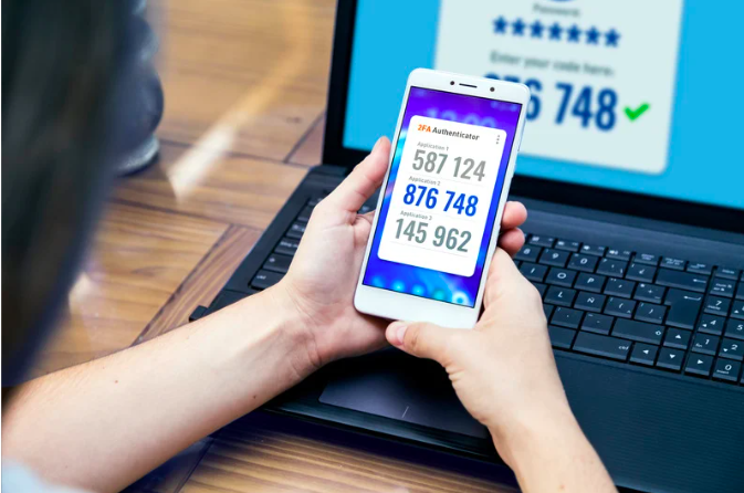 Person holding a smartphone displaying a two-factor authentication code in front of a laptop.