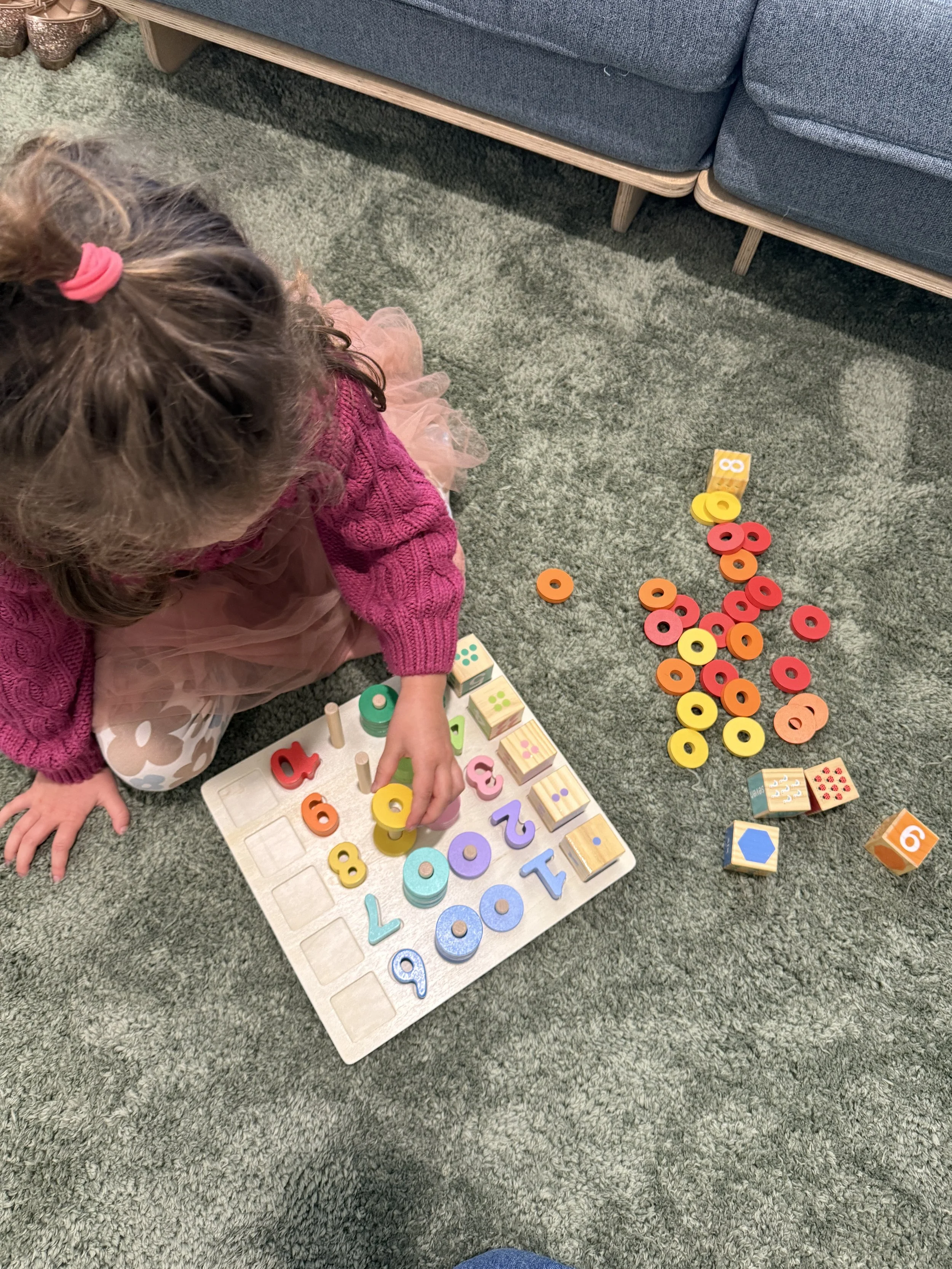 A young girl playing with colorful educational toys on a carpeted floor near a blue couch.