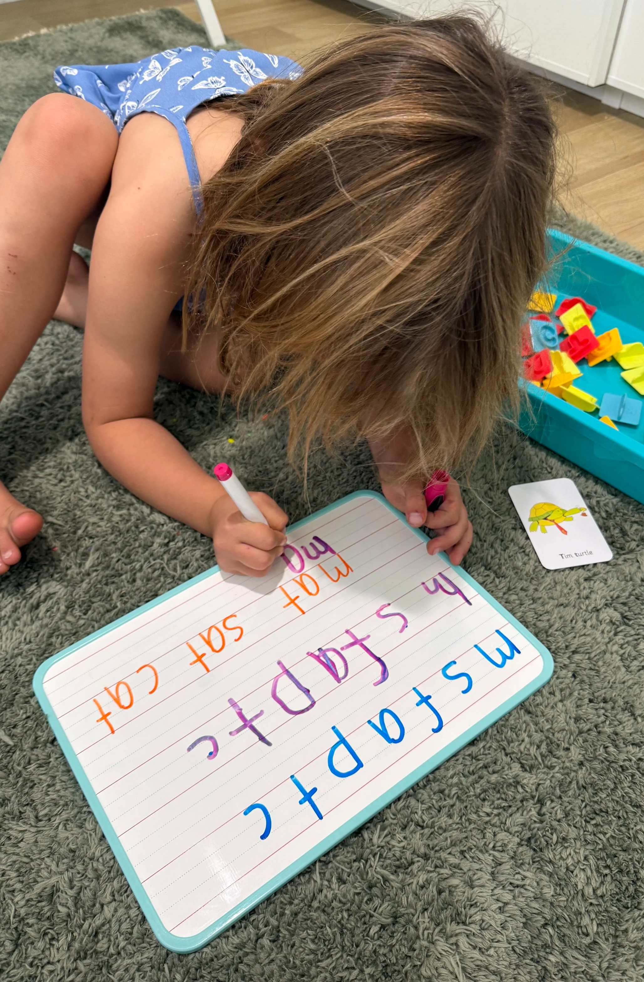 Child writing on a whiteboard with colorful markers, practicing writing the phrase 'I saw a turtle'
